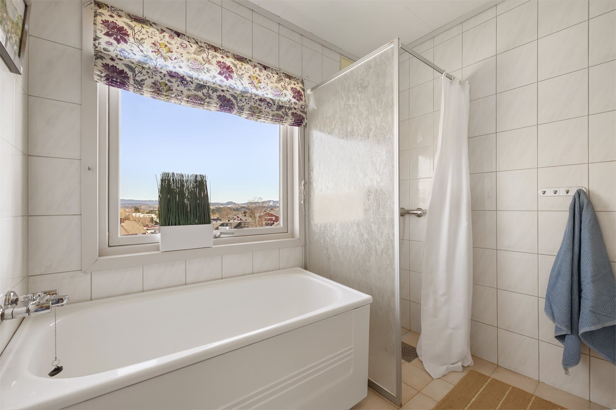 Lyst baderom utstyrt med dusjhjørne, badekar, servantinnrending og speil.