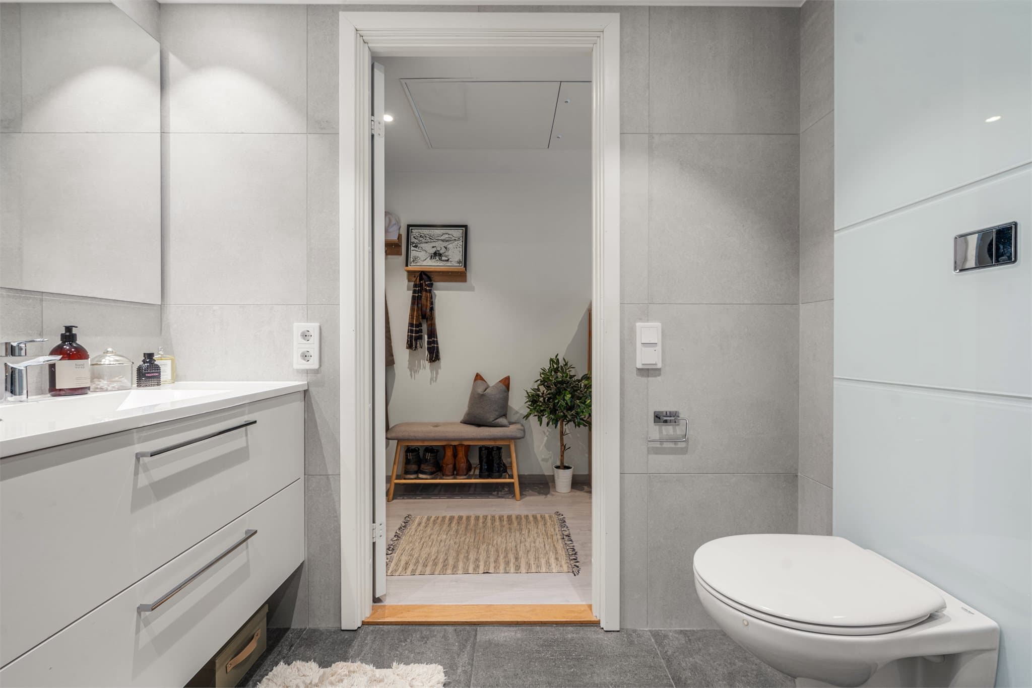 Baderommet har dusjløsning med regnfall, vegghengt toalett, servant på skuffeseksjon og overspeil.