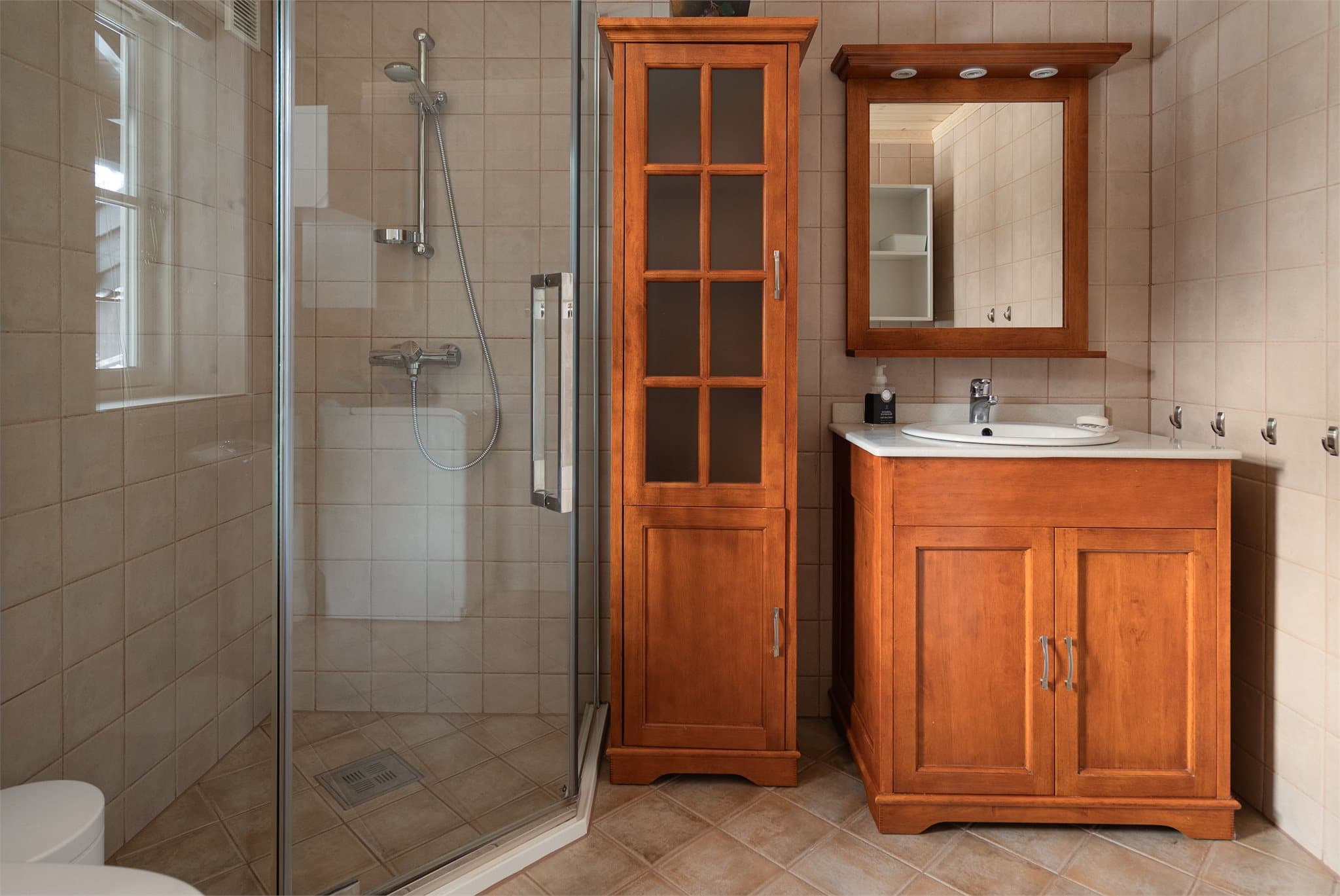 Flislagt bad med dusjhjørne, servantinnredning, speil, toalett og opplegg for vaskemaskin.