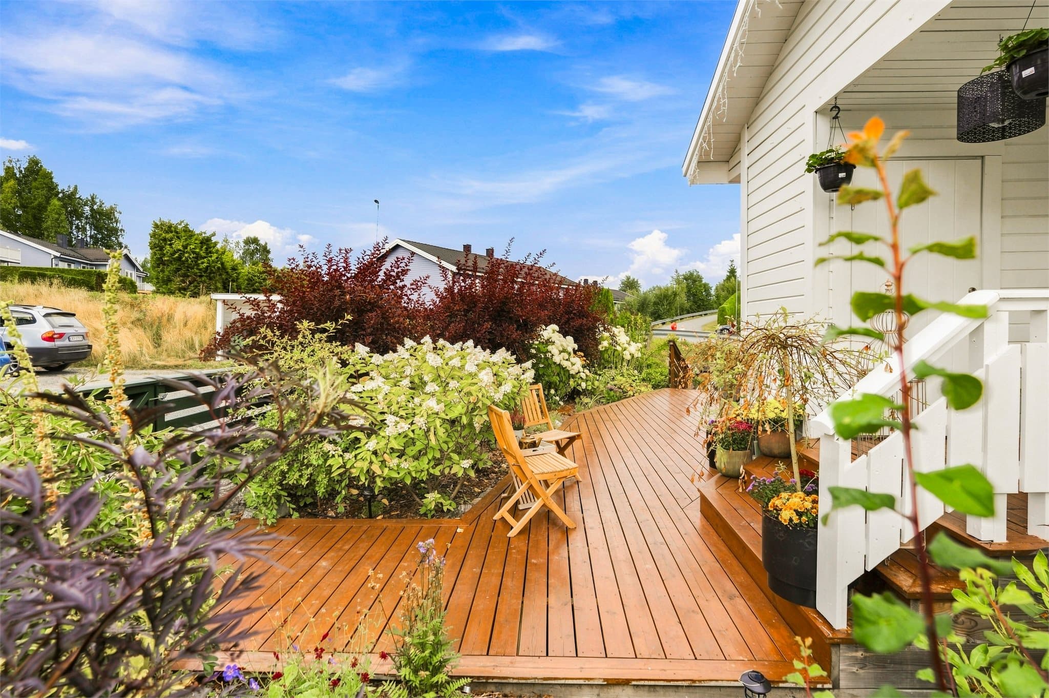 Et nydelig og velstelt uteområde med terrasseplatting, blomstrende bed og flere naturlige sitteplasser.