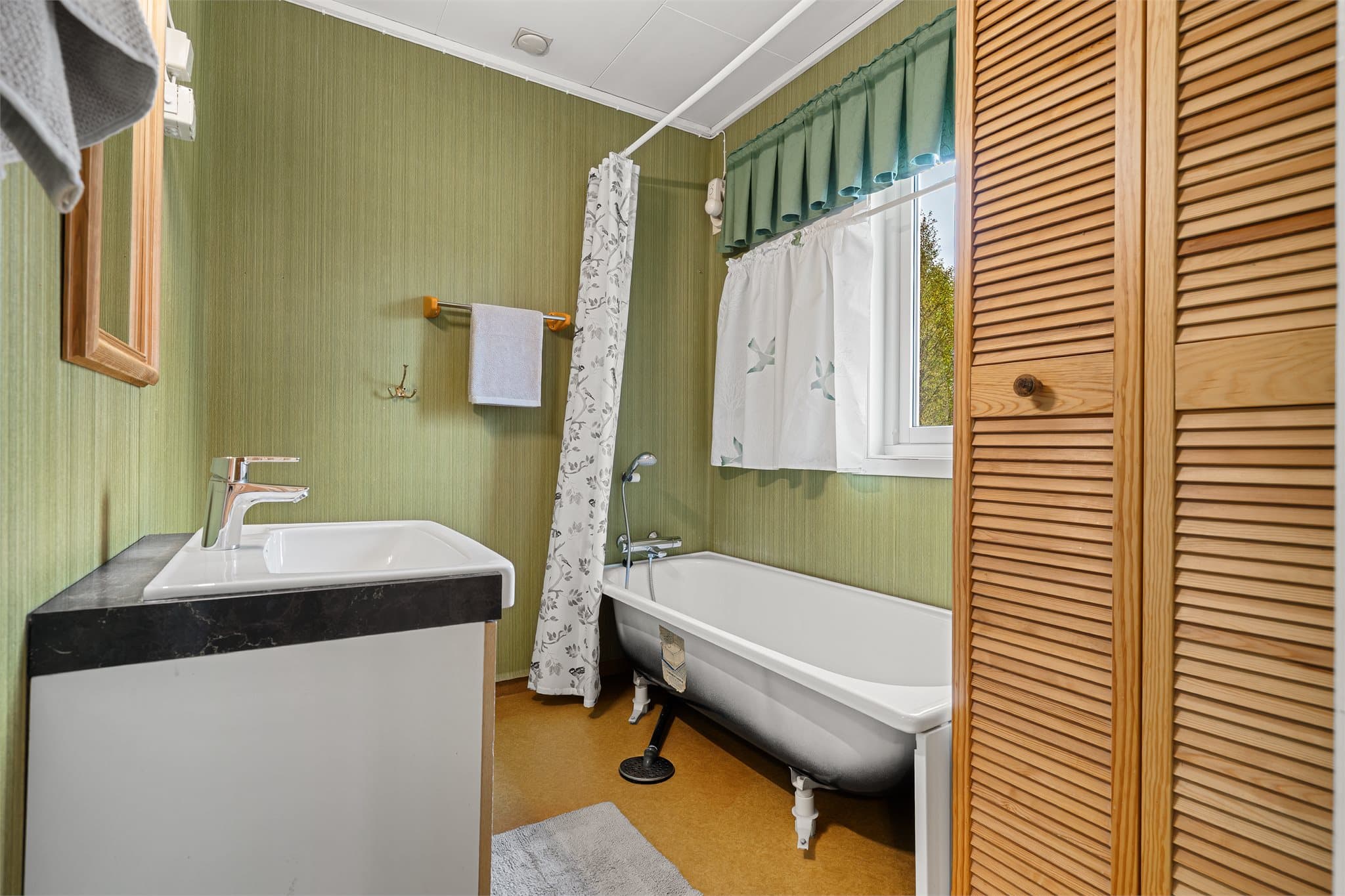 Bad i hovedetasjen innredet med badekar, baderomsinnredning og våtromsbelegg.