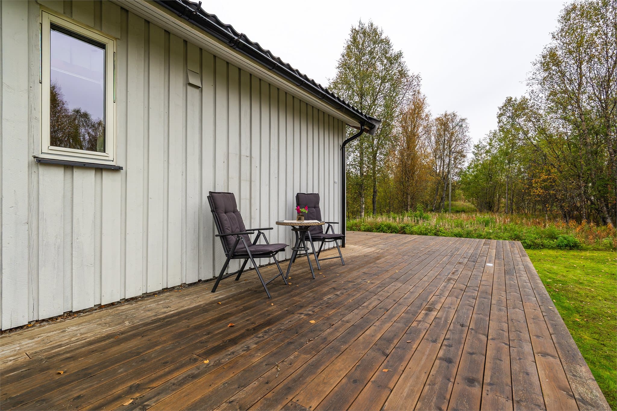 Trebearbeidet platting på bakkenivå som grenser mot hage og plenareal.