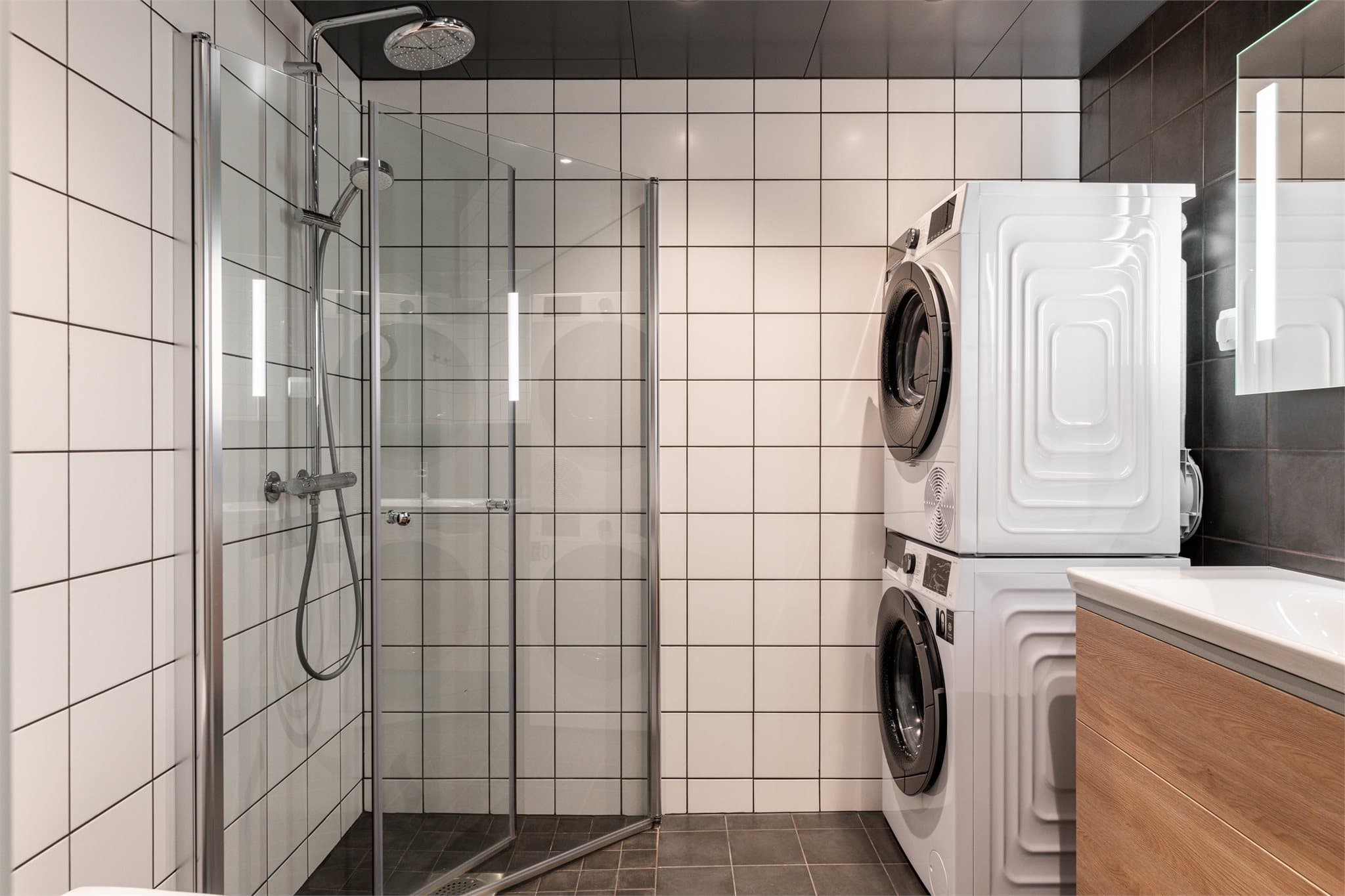 Badet er flislagt med hvite fliser på veggene og mørke fliser på gulvet, og sort himling.