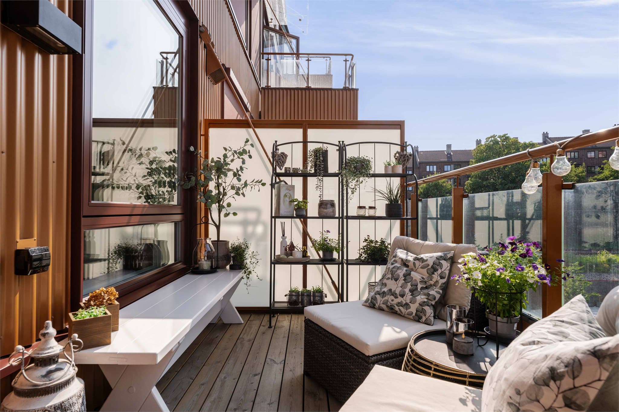 Balkongen har plass til en loungegruppe med bord og gir utsyn over fellesarealet og grøntanlegget nedenfor. En hvit skjermvegg på den ene siden gir noe le.