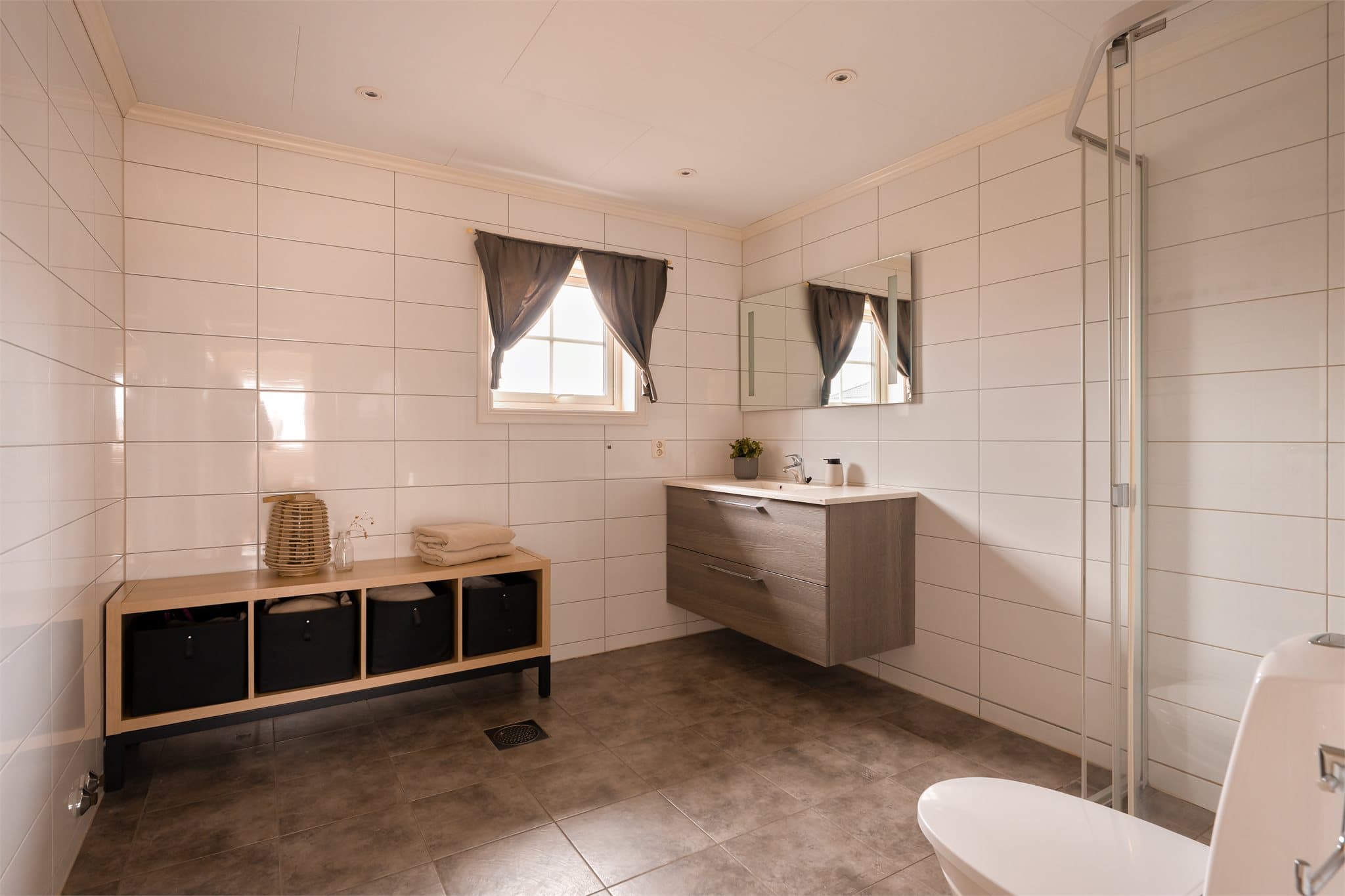 Delikat og romslig bad med dusjhjørne, gulvstående toalett og servant.