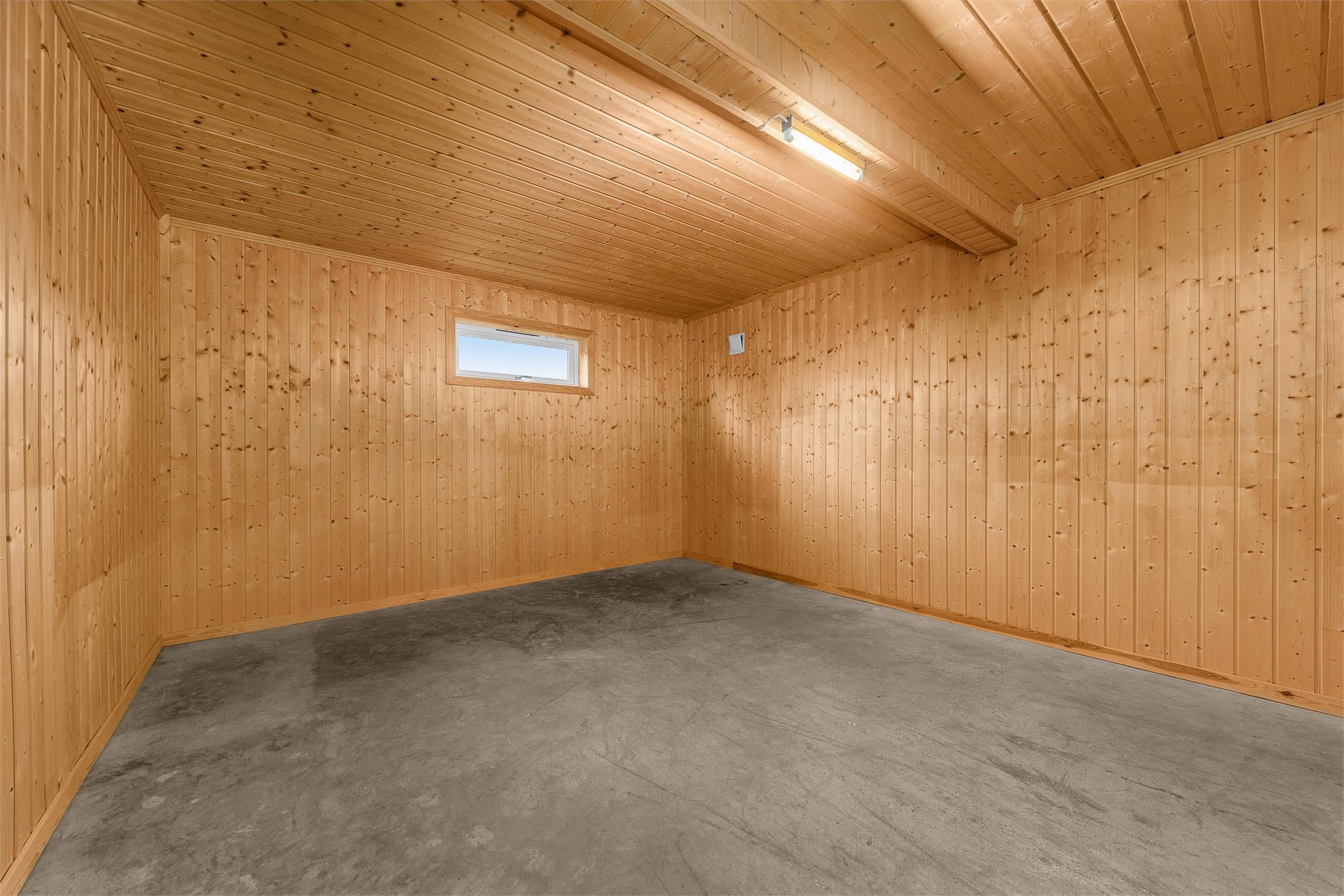 Kjellerboden har betonggulv, panelte vegger og lysinnslipp fra vindu.