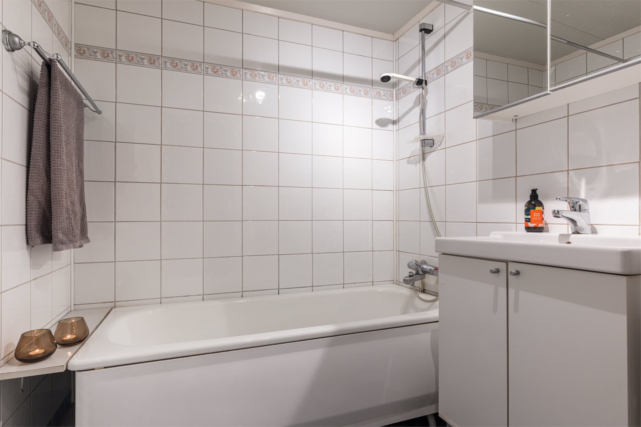 Lyst, flislagt baderom med badekar og servant.