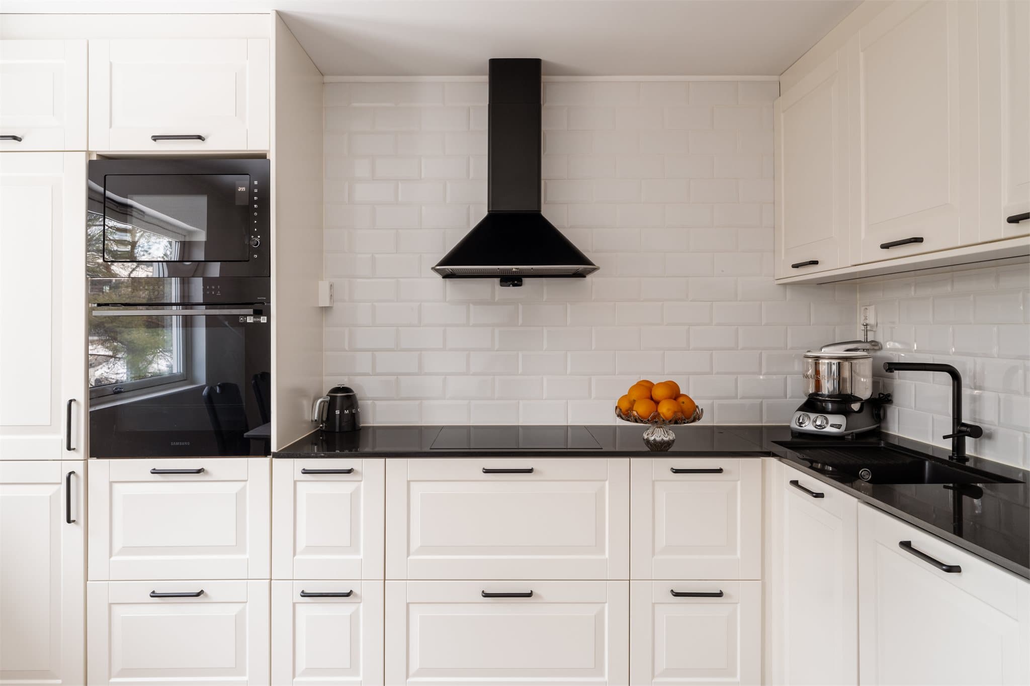 Kjøkkenet har mørk komposittbenkeplate og fliser mellom benk og overskap.