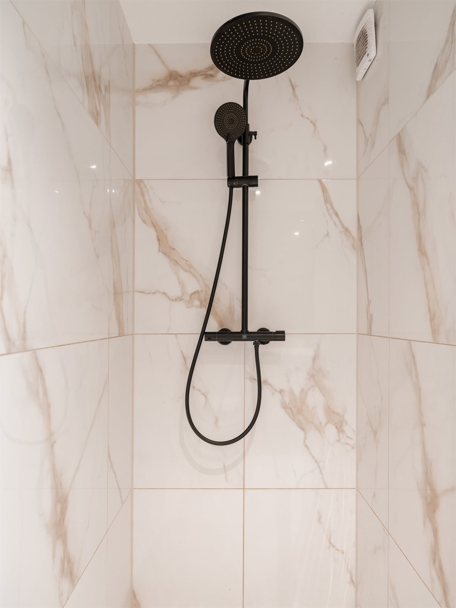 Badet er utstyrt med dusj på gulv og sorte detaljer som gir et gjennomført uttrykk.