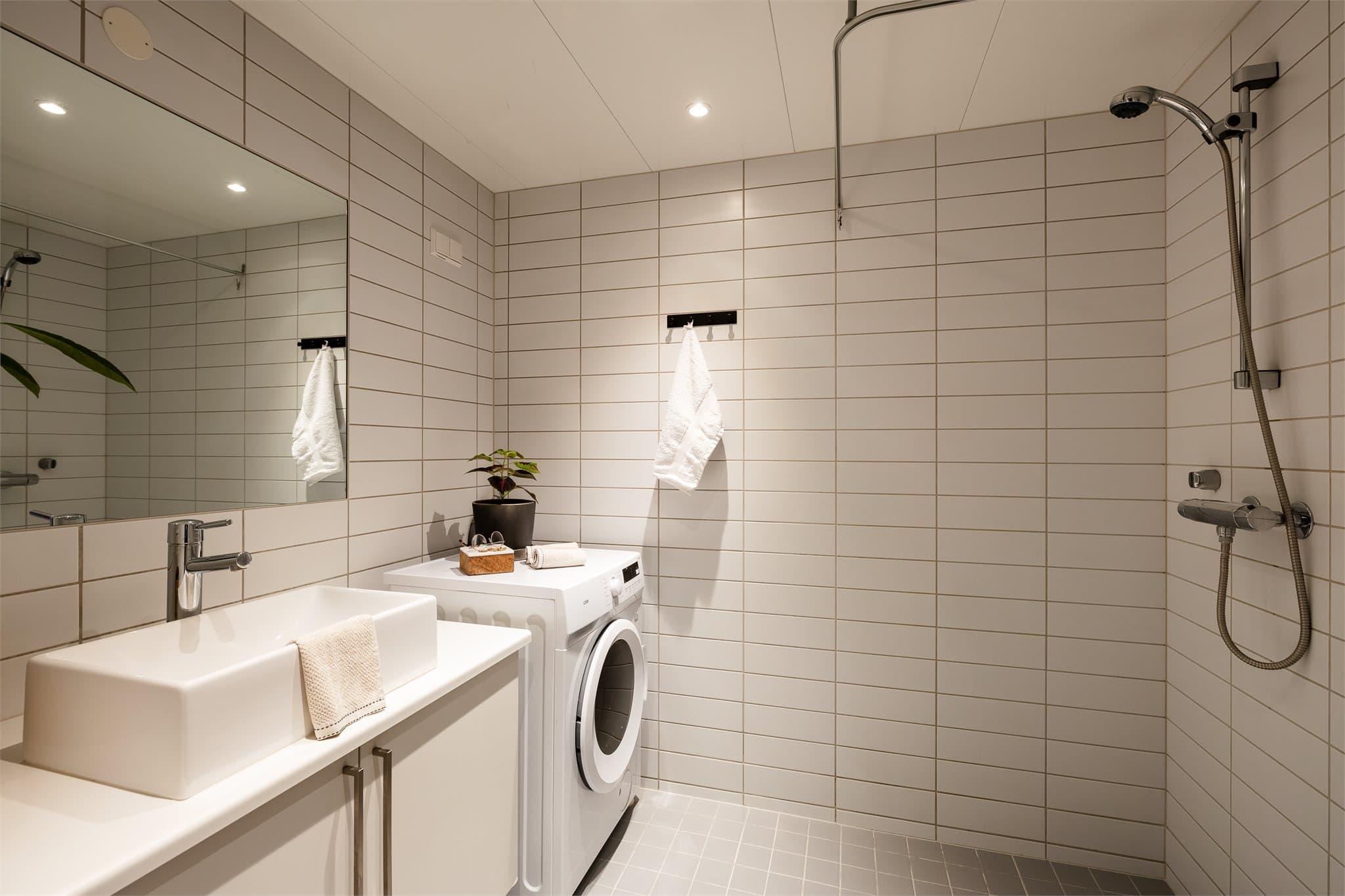 Badet har lyse flislagte overflater og opplegg for vaskemaskin.