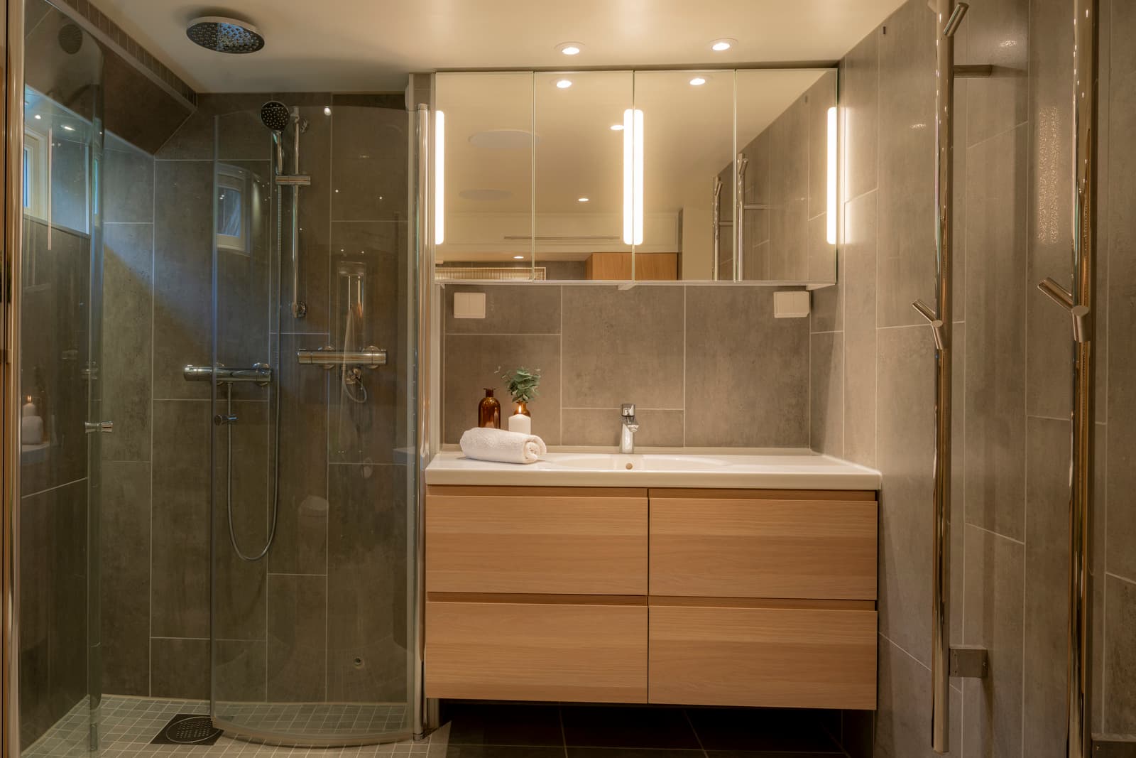 Videre er badet innredet med en bred servantløsning på en dobbel skuffeinnredning og tilhørende høyskap i moderne, lys eik. Dette gir både et varmt, nordisk preg og gode oppbevaringsmuligheter.