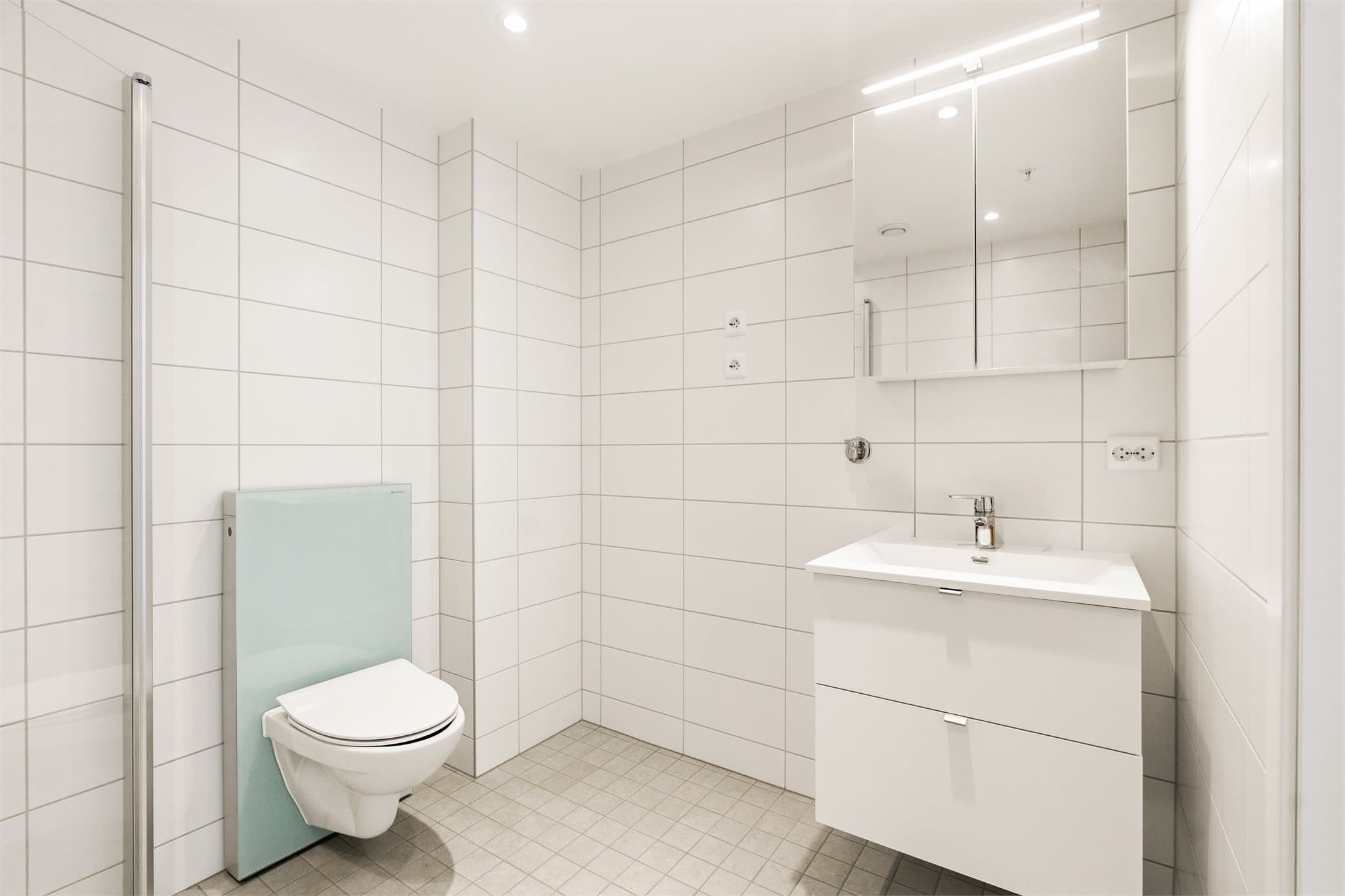 Badet er utstyrt med dusj med innfellbare dusjdører, toalett og baderomsinnredning med hvite fronter, og opplegg for vaskemaskin.