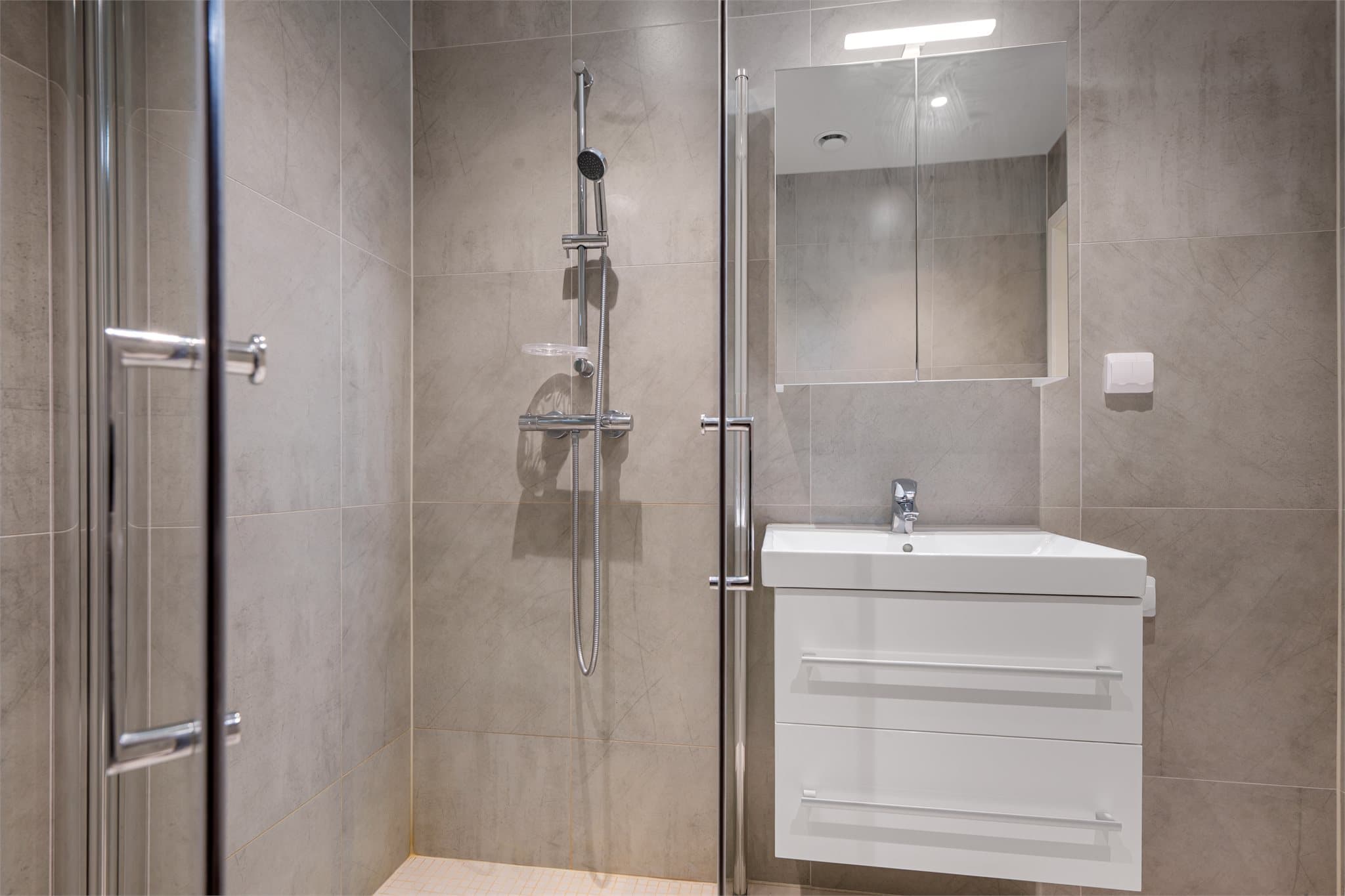 Badet er innredet med helservant på skuffeseksjon, speilskap, dusjhjørne og vegghengt toalett. Opplegg for vaskemaskin.