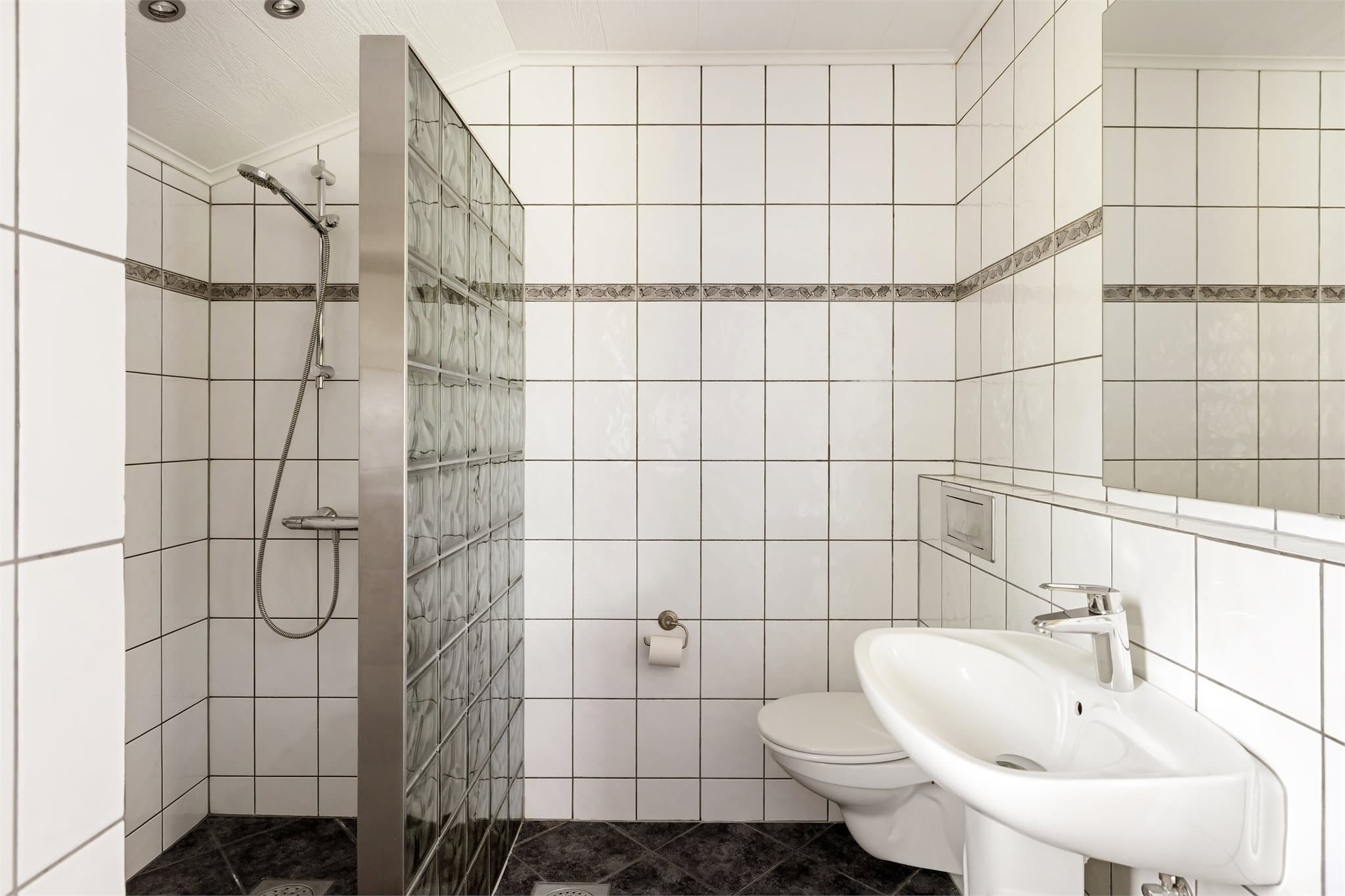 Baderomsinnredning med søyleservant m/ett-greps blandebatteri, speil, vegghengt toalett, veggskap og dusjnisje vegg av glassbyggerstein samt dusjgarnityr med hånddusj