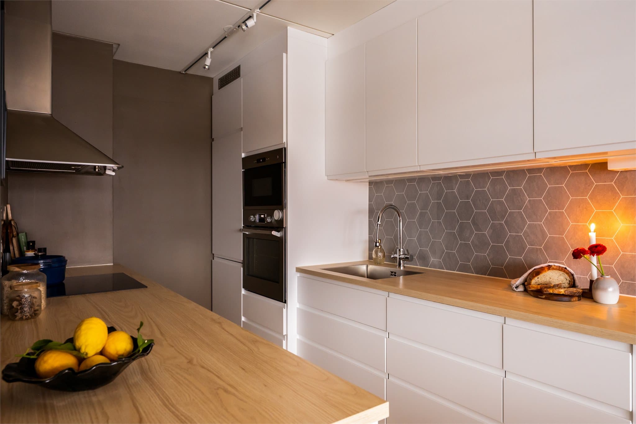 Innredning med glatte, fabrikklakkerte fronter og laminatbenkeplate med planlimt kum i rustfritt stål. Stålplate bak platetopp og belysning under overskap gir både funksjon og et stilrent preg.