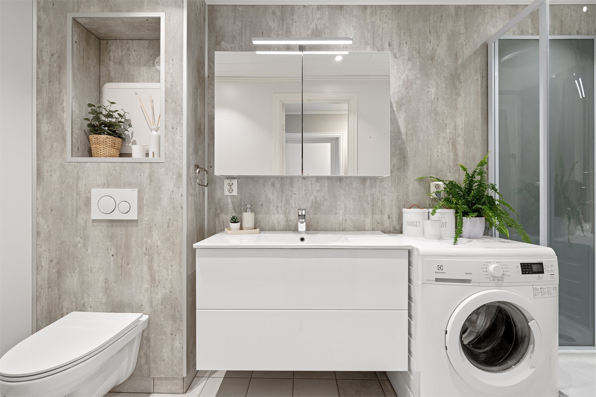 Tidløst baderom utstyrt med varmekabler i gulv, vegghengt toalett, servantinnredning, speil med lys, høyskap og dusjkabinett.