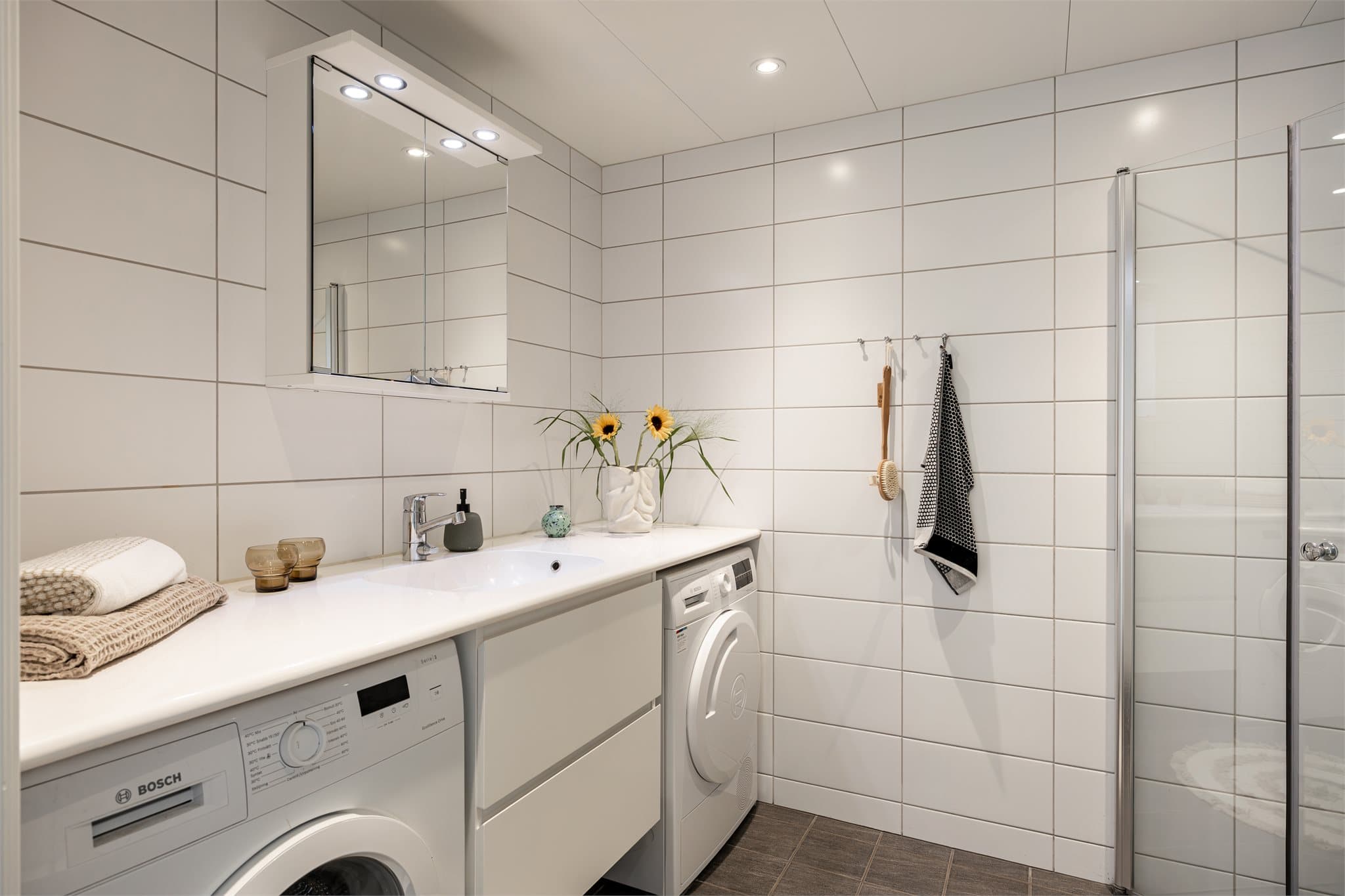 Et delikat og flislagt baderom med opplegg for vaskemaskin, gulvvarme og downlights i taket.