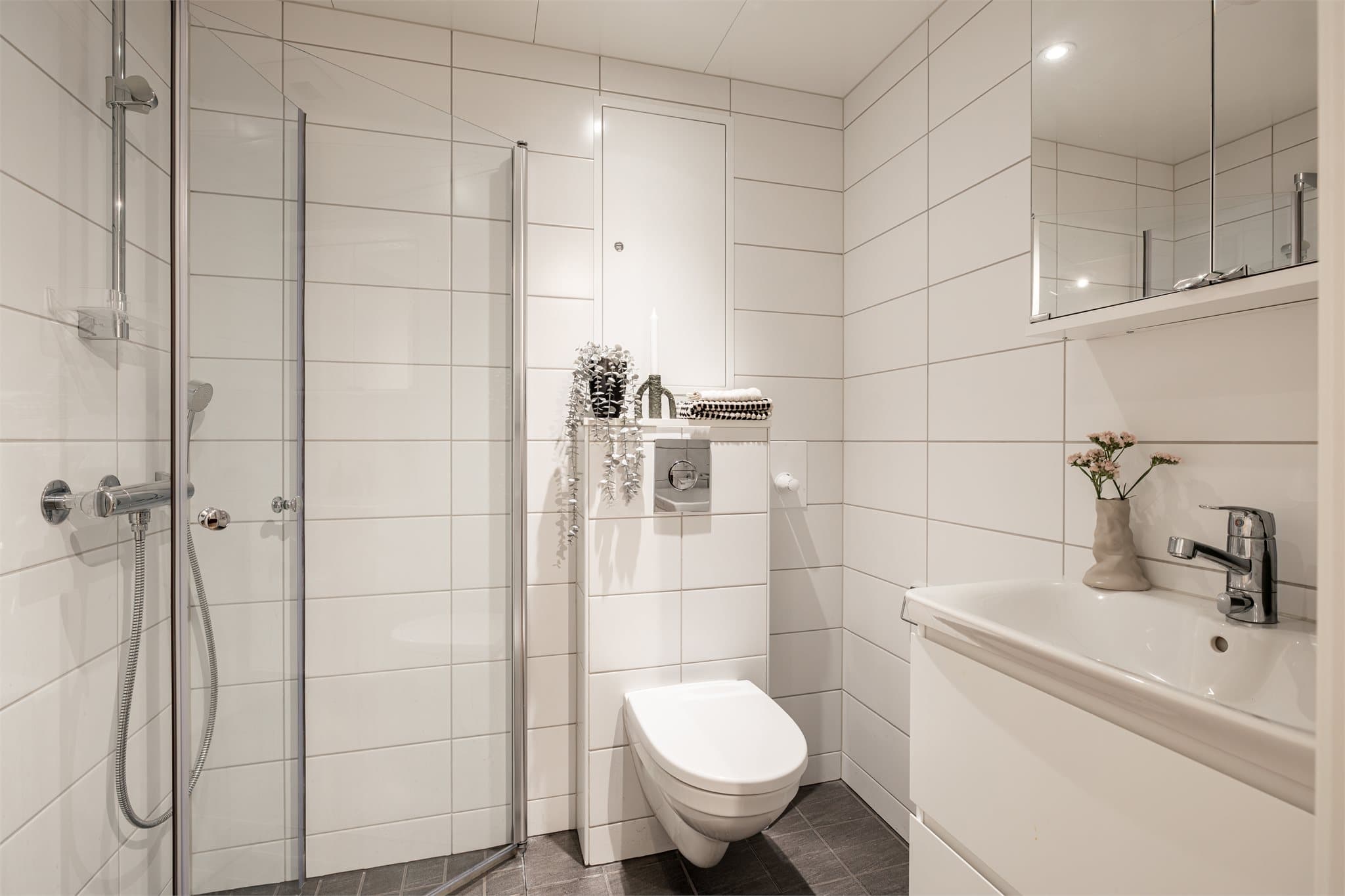 Gangen har direkte tilgang til gjestebadet med dusj, toalett og god oppbevaringsplass i både speilskap og skuffer under vasken. Det er gulvvarme og downlights i taket også her.