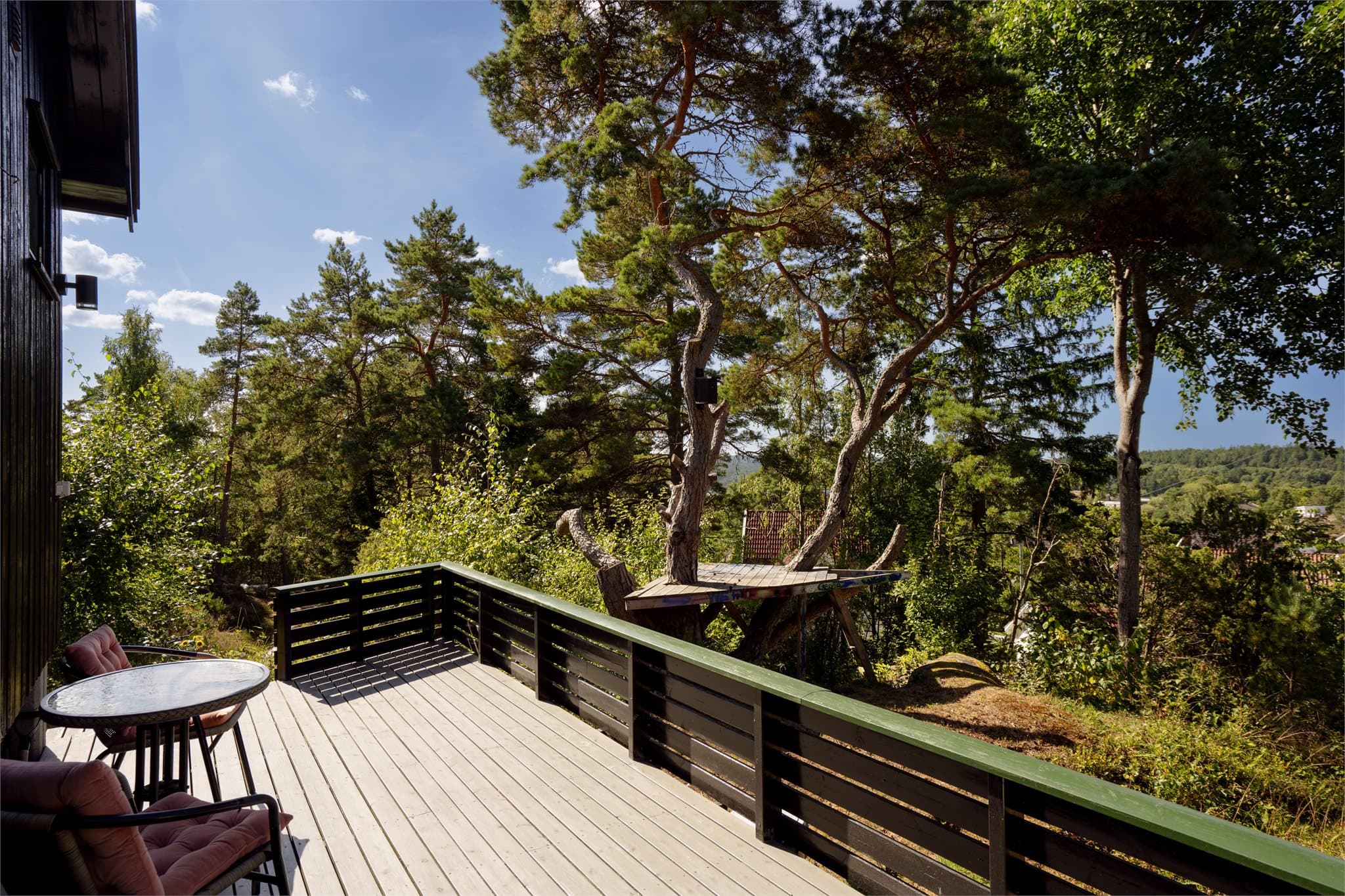 Rekkverk i tre rammer inn terrassen med utsikt mot naturen.