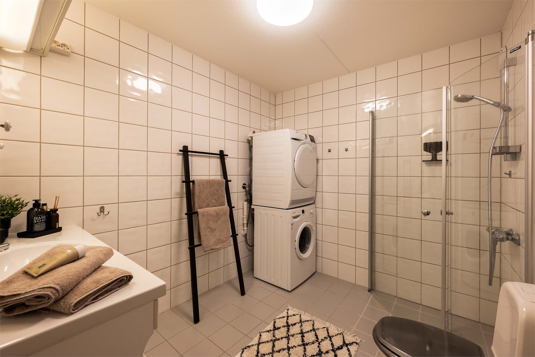 Tidløst og lyst baderom fra byggeår. Rommet er innredet med baderomsinnredning, gulvmontert toalett og dusjhjørne med svingdører.