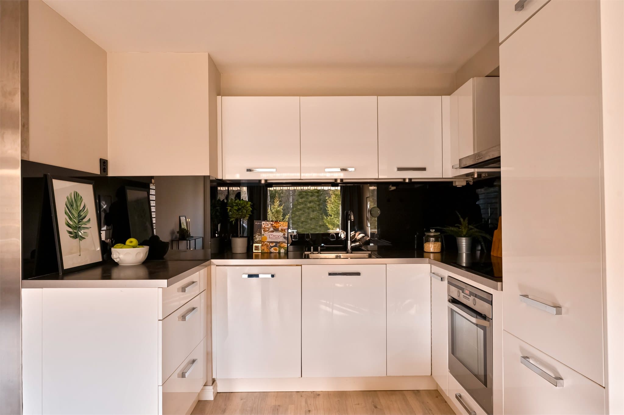 Benkeplaten er i laminat og har en planlimt kum i rustfritt stål. Over benkeplaten er det montert glassplater på vegg, og det er belysning under overskapene som gir godt arbeidslys.