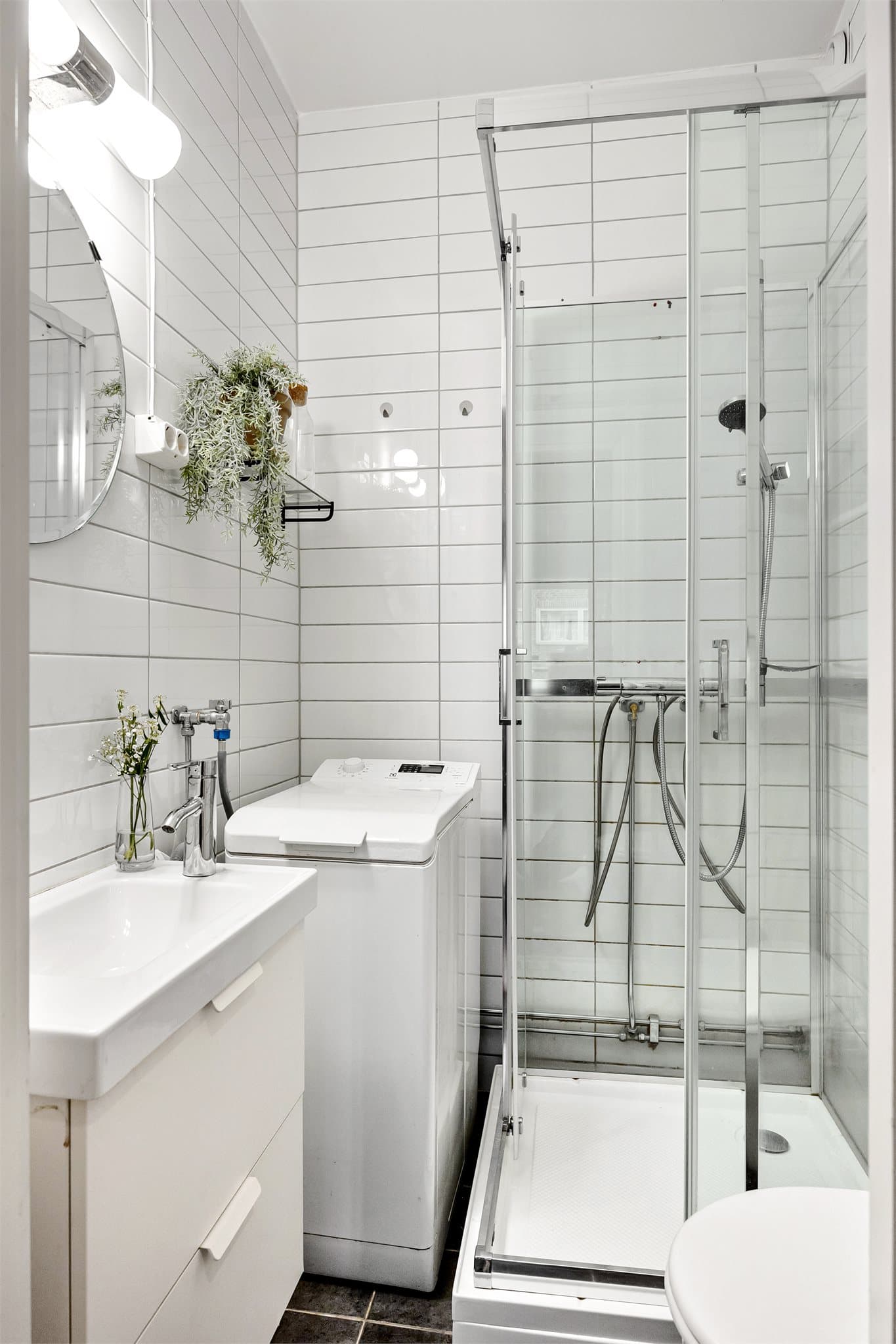 Tidløst flislagt baderom med dusjkabinett og opplegg for vaskemaskin.