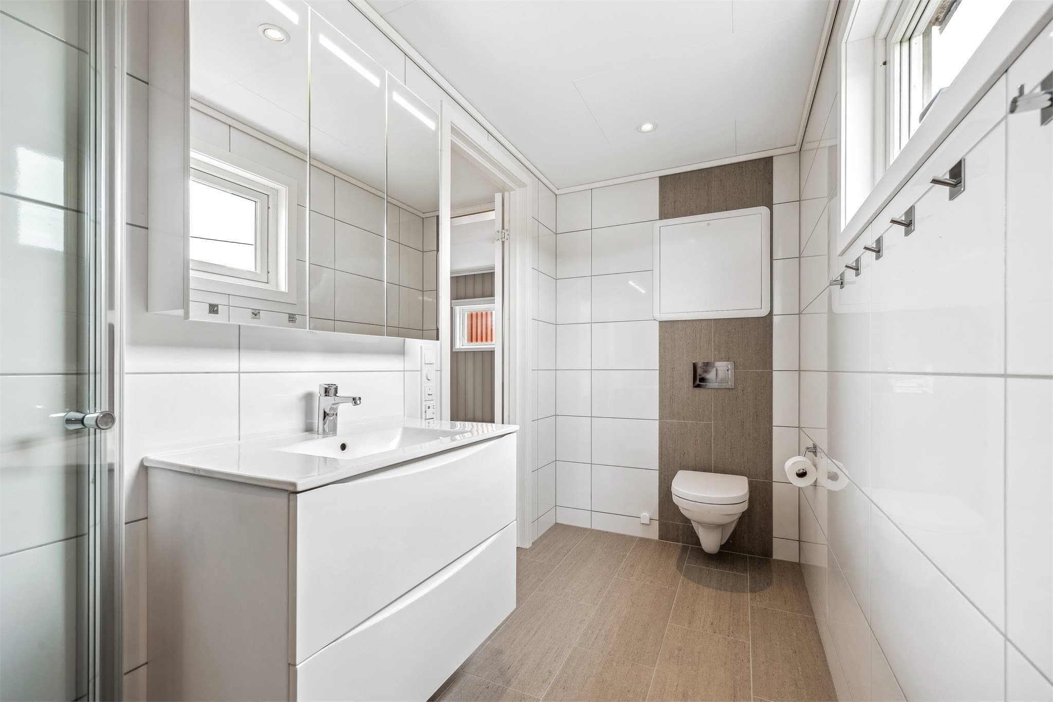 Badet har moderne innredning med servant, speilskap med belysning, vegghengt toalett, dusjhjørne og downlights i himling samt gulvvarme.