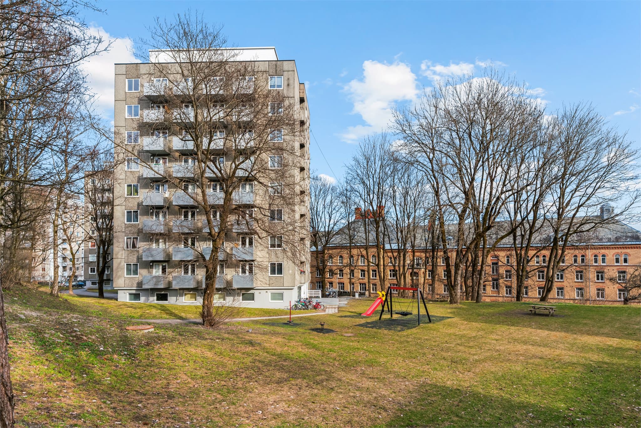 Store, grønne fellesarealer med lekeplass og sittegrupper omkranser bygget.