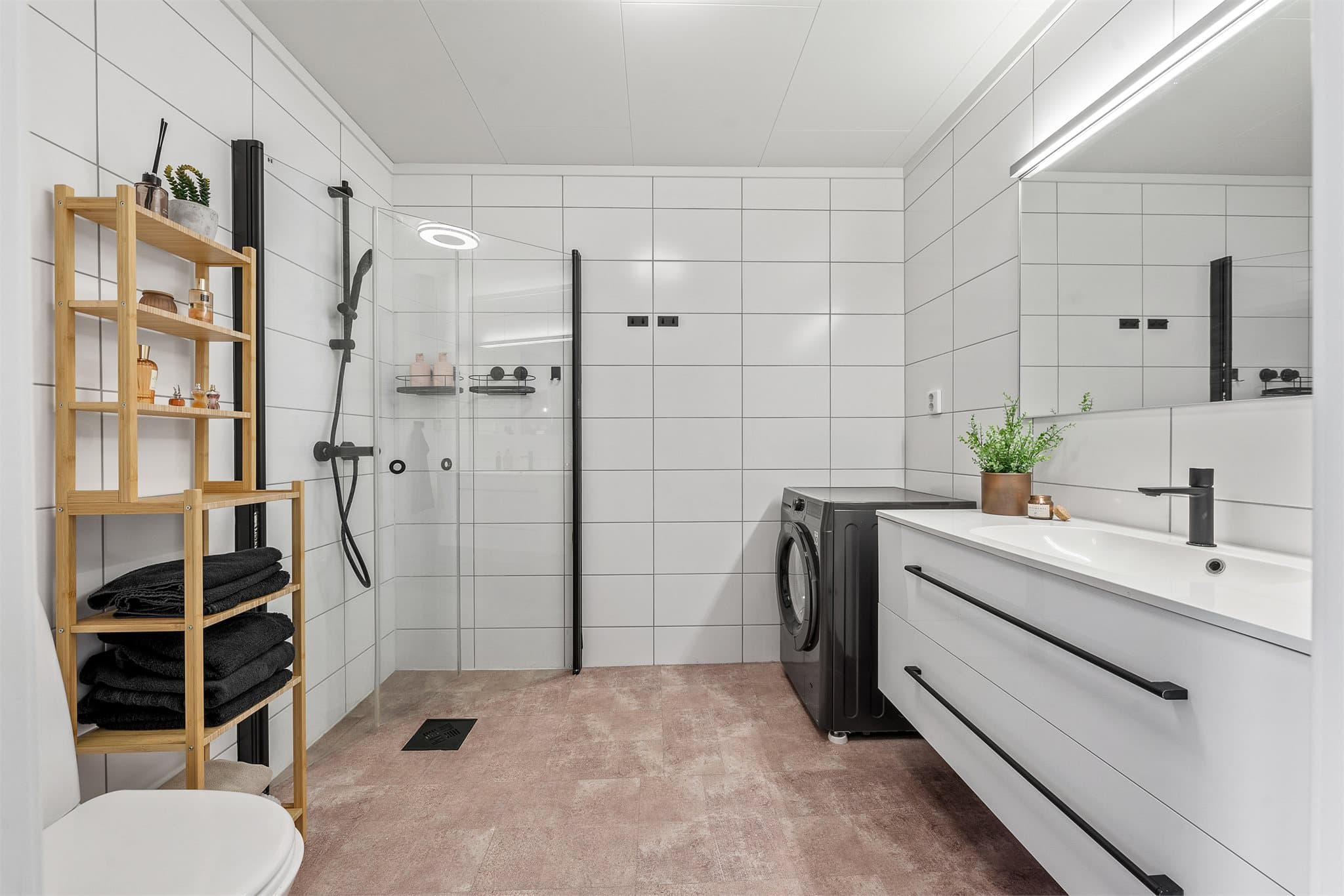 Pent baderom med lyse fliser på vegg og vinylbelegg over fliser på gulv.