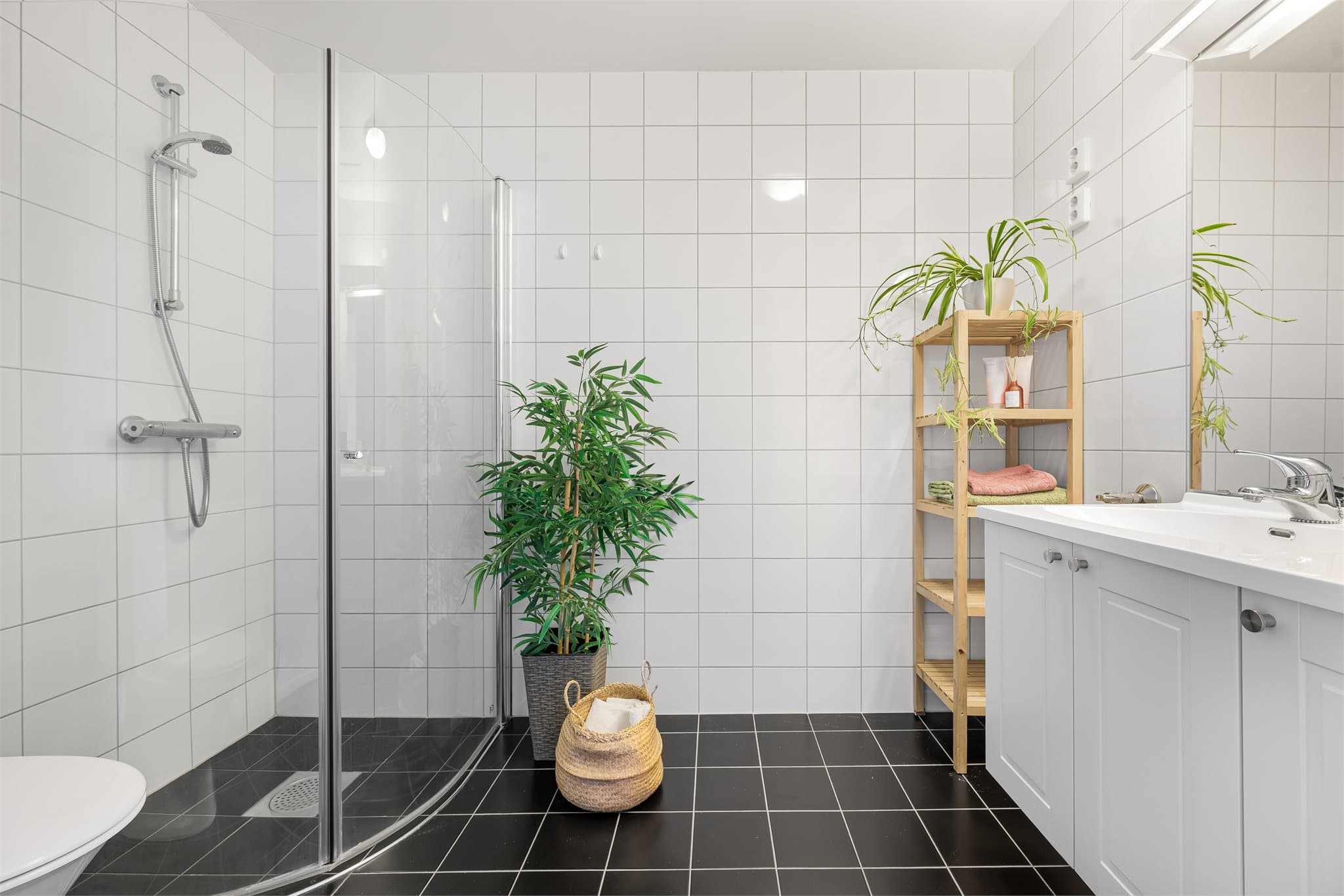 Badet fremstår funksjonelt og stilrent med innfellbare dusjvegger i herdet glass, helservant på innredning, klosett, gulvvarme og praktisk opplegg for vaskemaskin og tørketrommel.