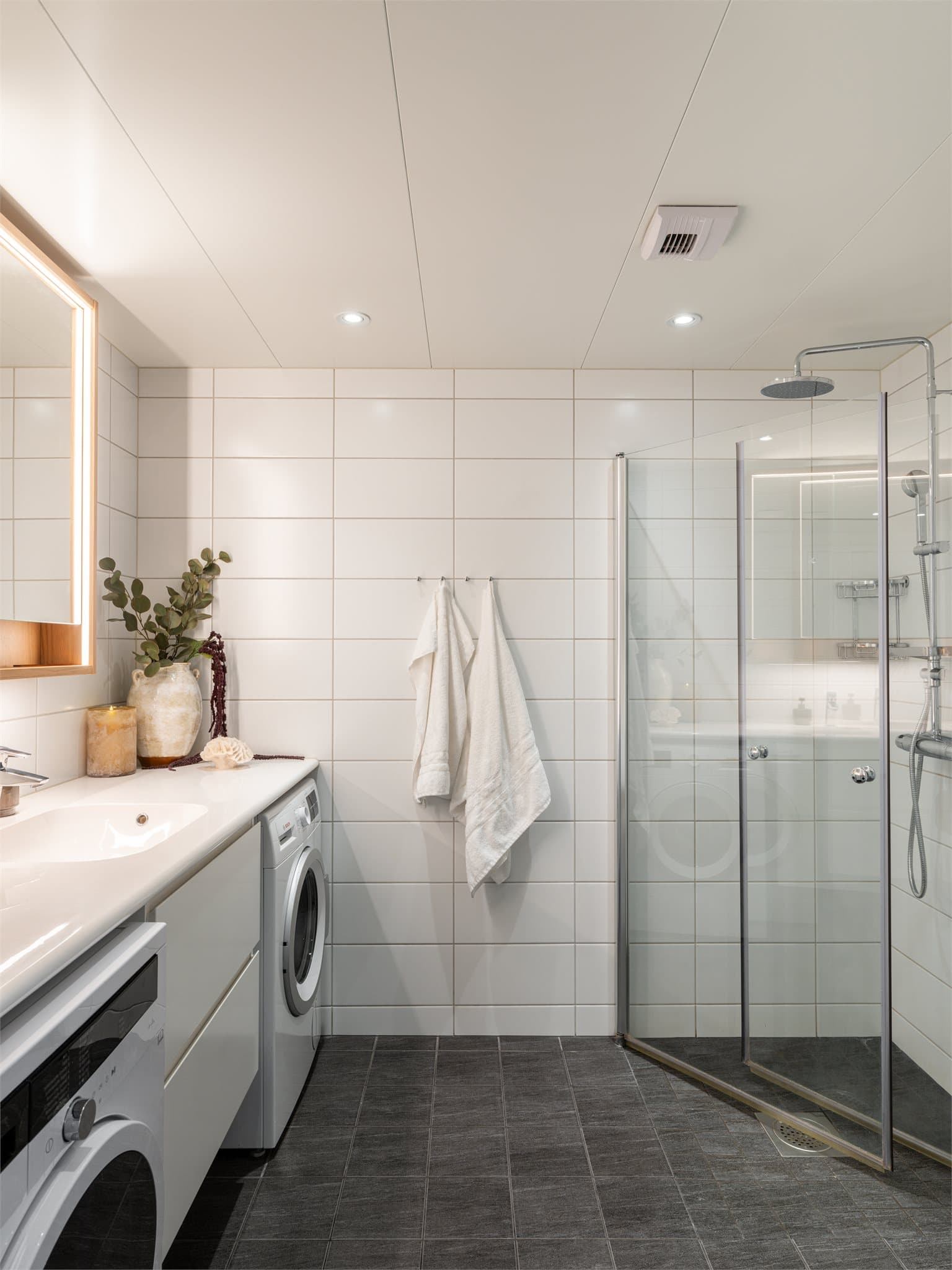 Flislagt bad med gulvvarme, innfelte downlights og dusjhjørne med svingbare glassdører.