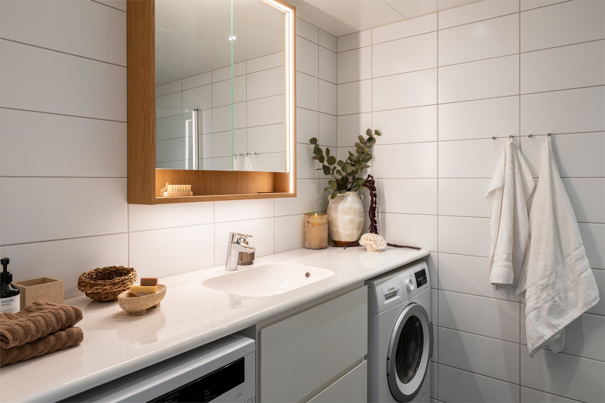 Badet er stilrent innredet med servant nedfelt i baderomsinnredning, lekkert speilskap, vegghengt toalett og dusjhjørne med svingbare glassdører. Det er opplegg for vaskemaskin og balansert ventilasjon.