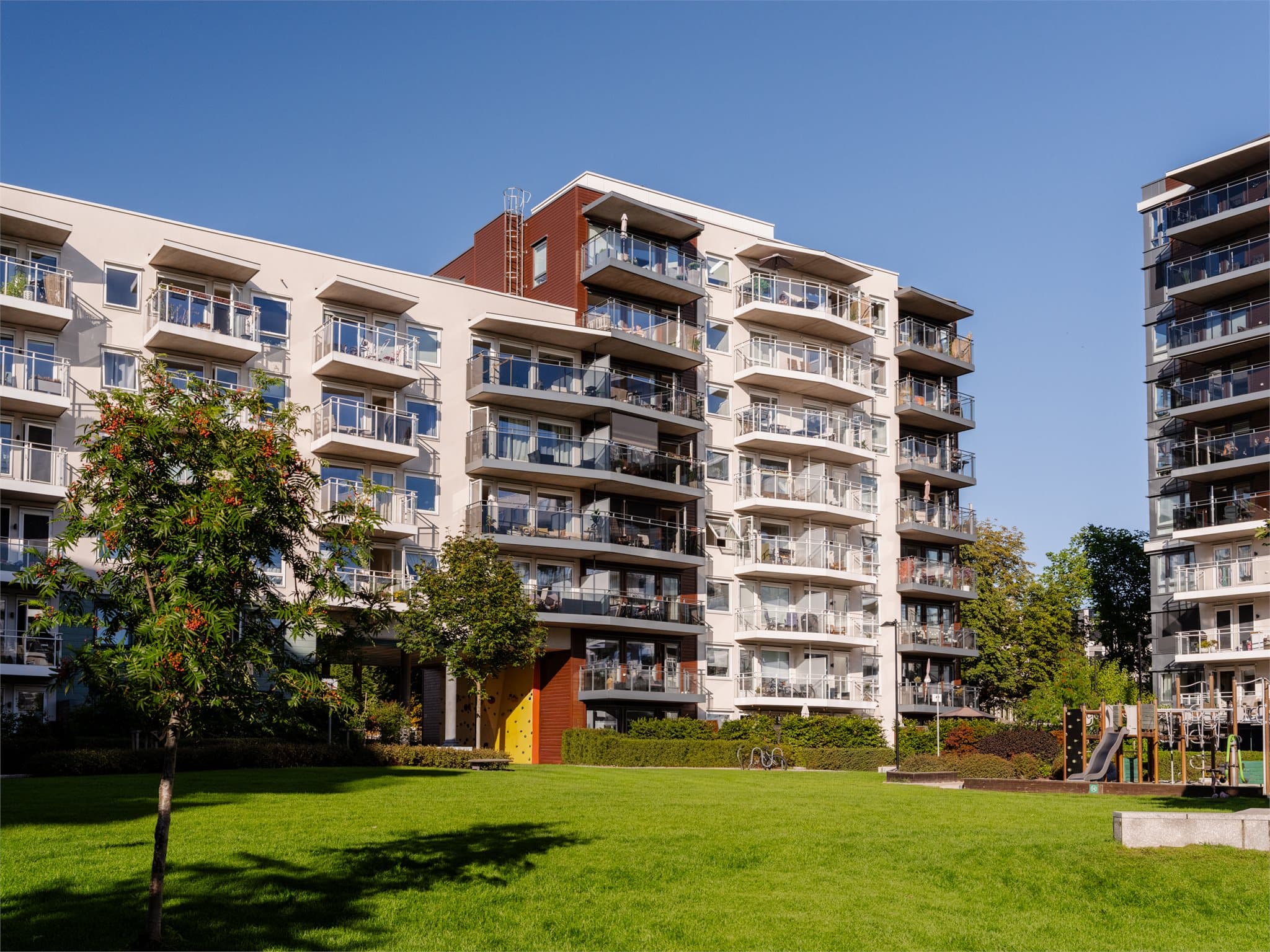 Boligblokk fra 2021 med pent opparbeidede fellesplener og lekeplass.