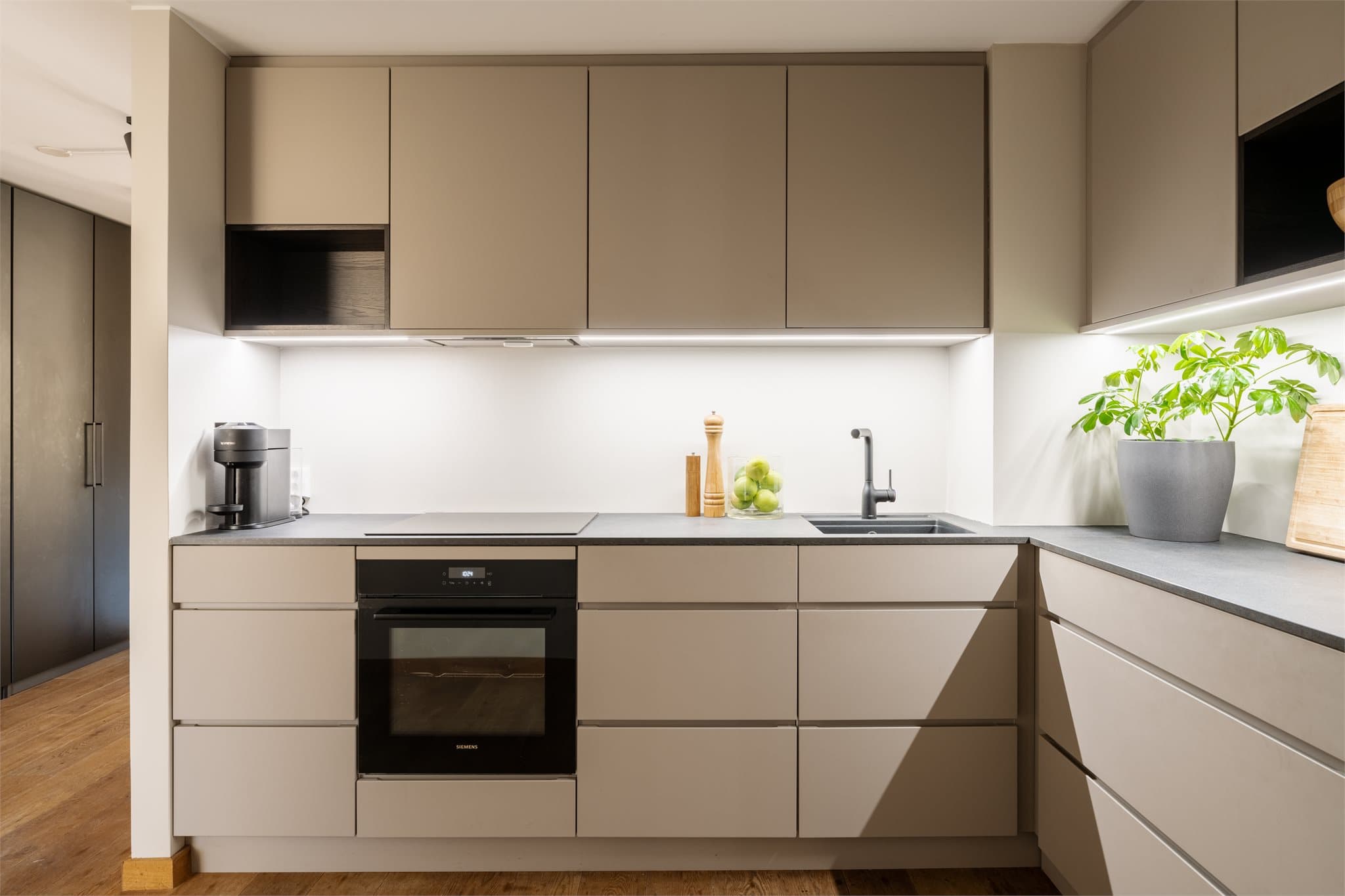 KVIK kjøkkeninnredning med glatte, folierte fronter, laminat benkeplate med planlimt kum i kompositt/plast og belysning via lyslist (LED) under overskap.
