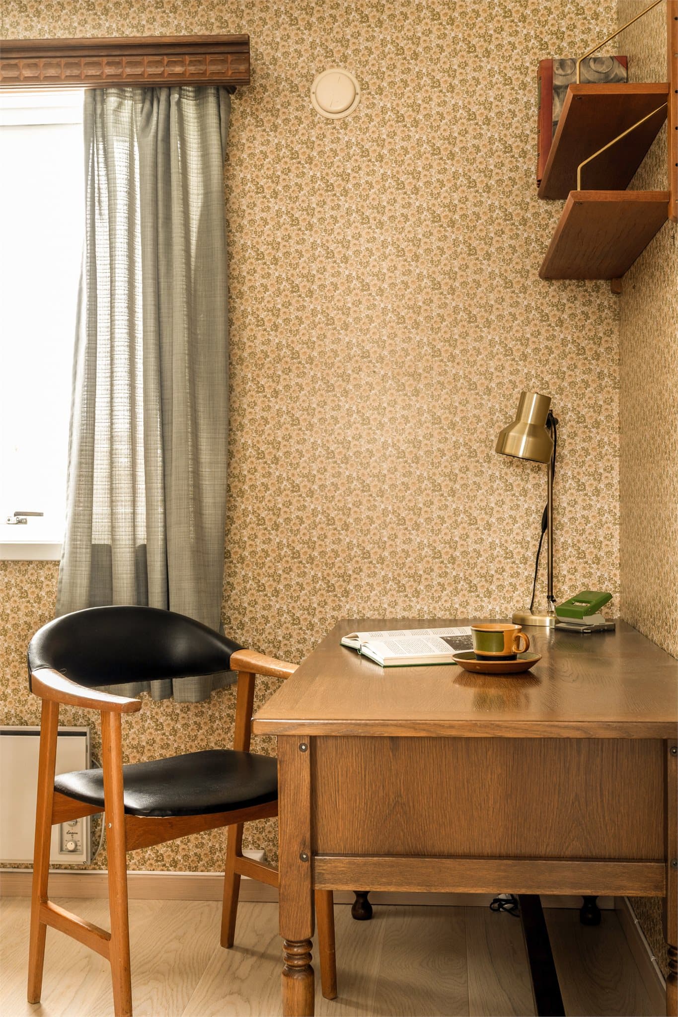 Fra spisestuen ledes du videre inn i boligens eget lille tidskapsel – kontoret. Her møter du blomstrete 1970 talls tapet som stolt brer seg over veggene, fullt av farger, former og den karakteristiske optimismen fra tiåret.