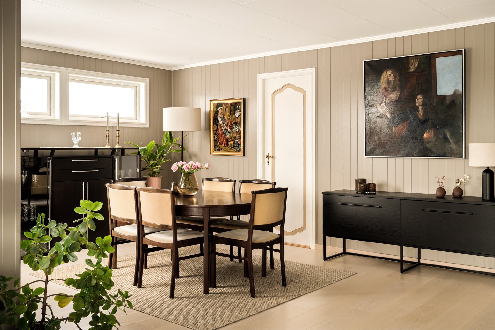 Spisestuen ligger i en naturlig forlengelse av stuen. Det lyse, moderniserte uttrykket videreføres også her, med de samme rolige veggflatene og det lyse gulvet som skaper en harmonisk helhet. Samtidig gir mørkere møbler rommet tyngde og kontrast.