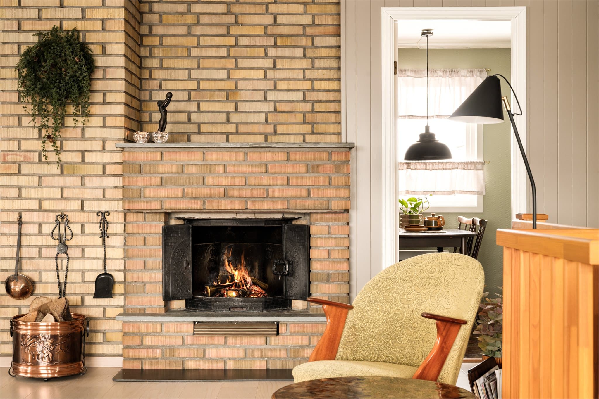 De solide teglsteinene gir rommet tyngde og karakter, med sin lune fargetone og levende overflate. Den rustikke fasaden binder rommene sammen på en lun og karakterfull måte, og skaper en rød tråd mellom kjøkkenets mørke tretoner og stuens lysere uttrykk.