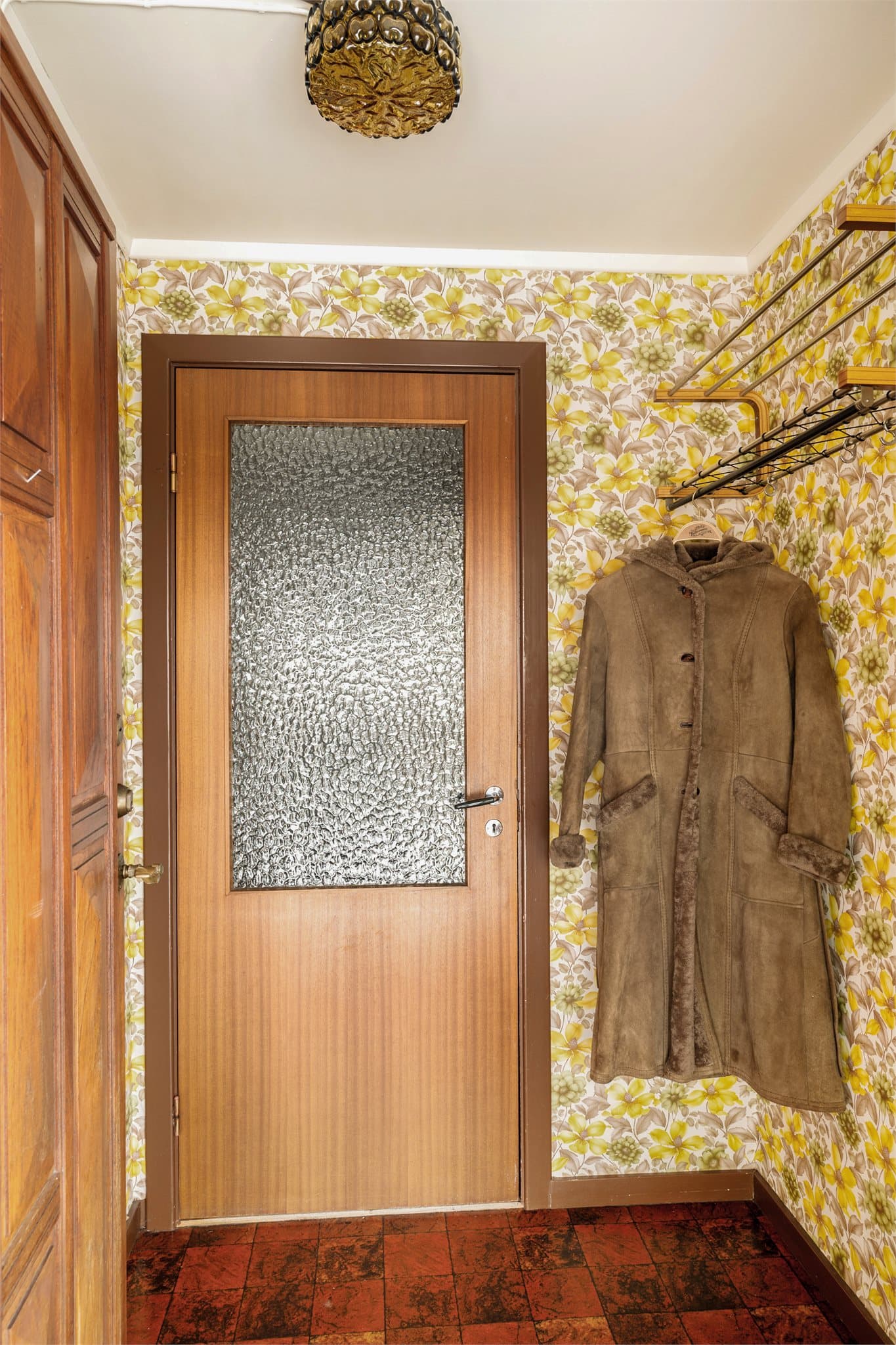 Det mørkerøde gulvbelegget, med sitt klassiske flisemønster, setter tonen idet du trer inn – lunt, karakterfullt og akkurat passe nostalgisk. Her møter du en solid teakdør som ønsker deg velkommen med den tyngden og varmen bare ekte treverk kan gi.