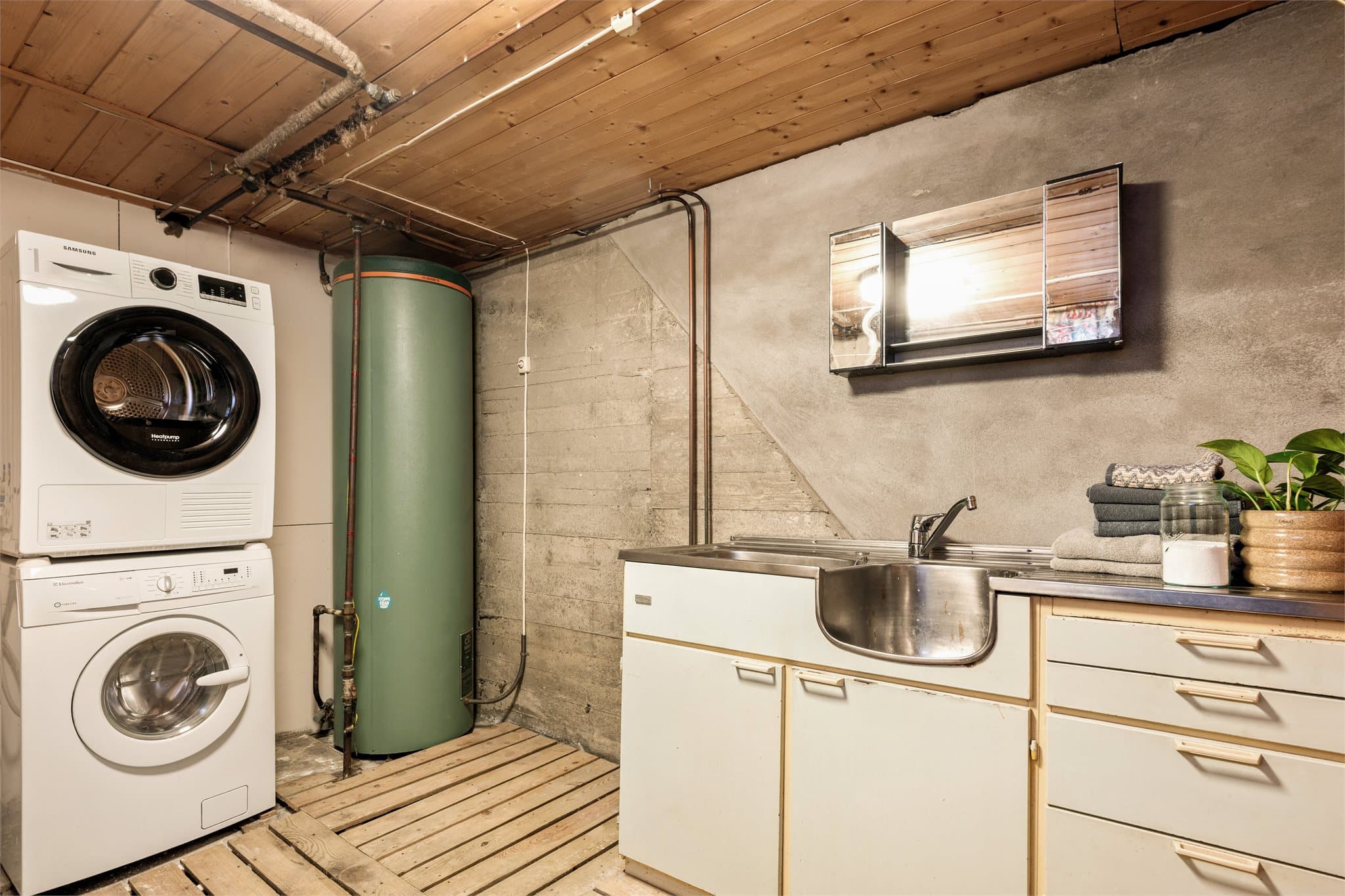 Betonggulvet er smart belagt med trepaller, som både luner og gir et mer behagelig underlag. Stråleovnen gir gode tørkemuligheter – et rom som er tilrettelagt for effektiv hverdagshåndtering, enten det gjelder klesvask eller våte ytterklær.