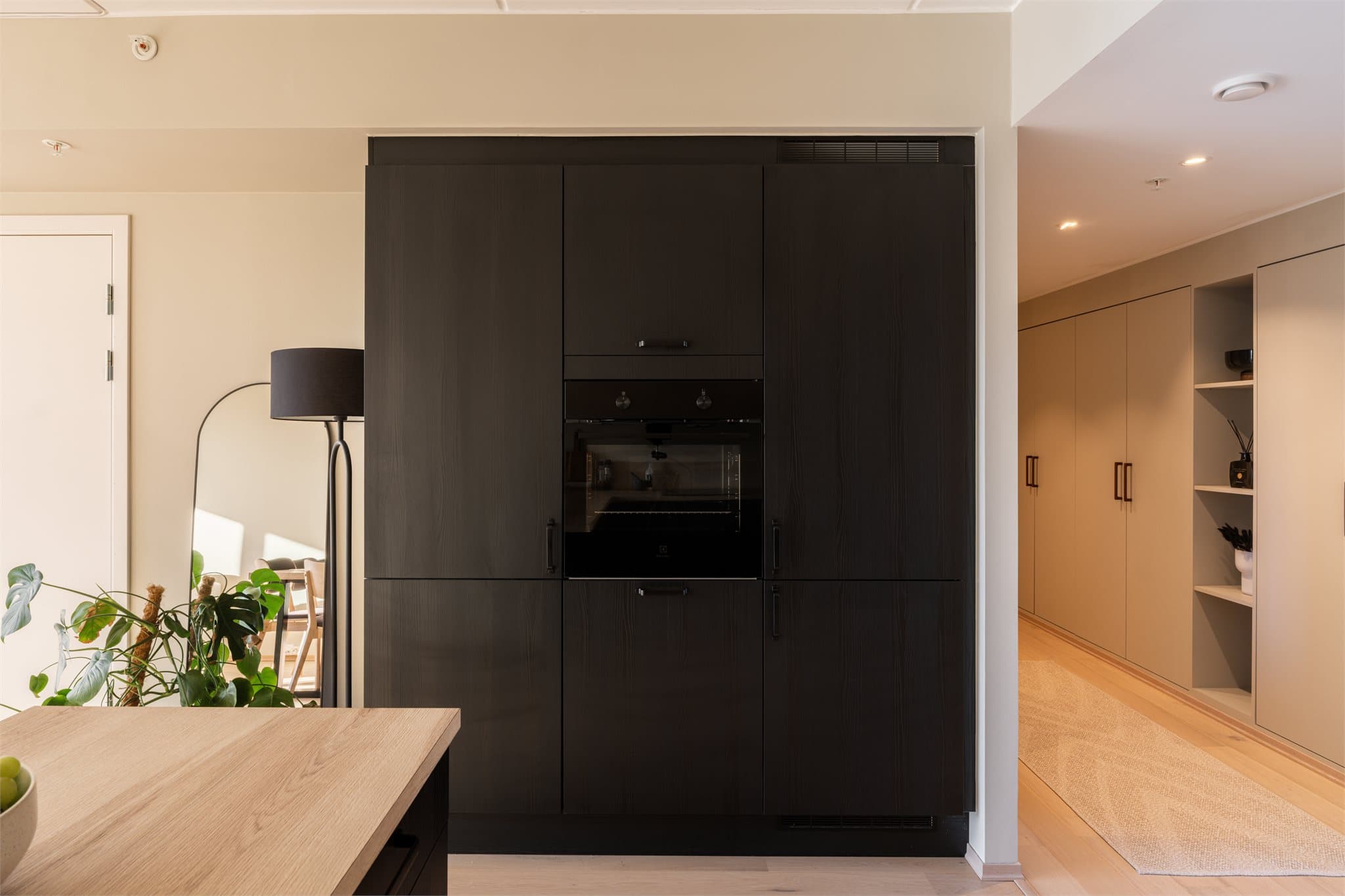 Stort høyskap i nisje på motsatt side av kjøkkeninnredningen som både gir ekstra lagring, i tillegg til at den gir en lekker og gjennomført følelse uten å "stjele" rommet.