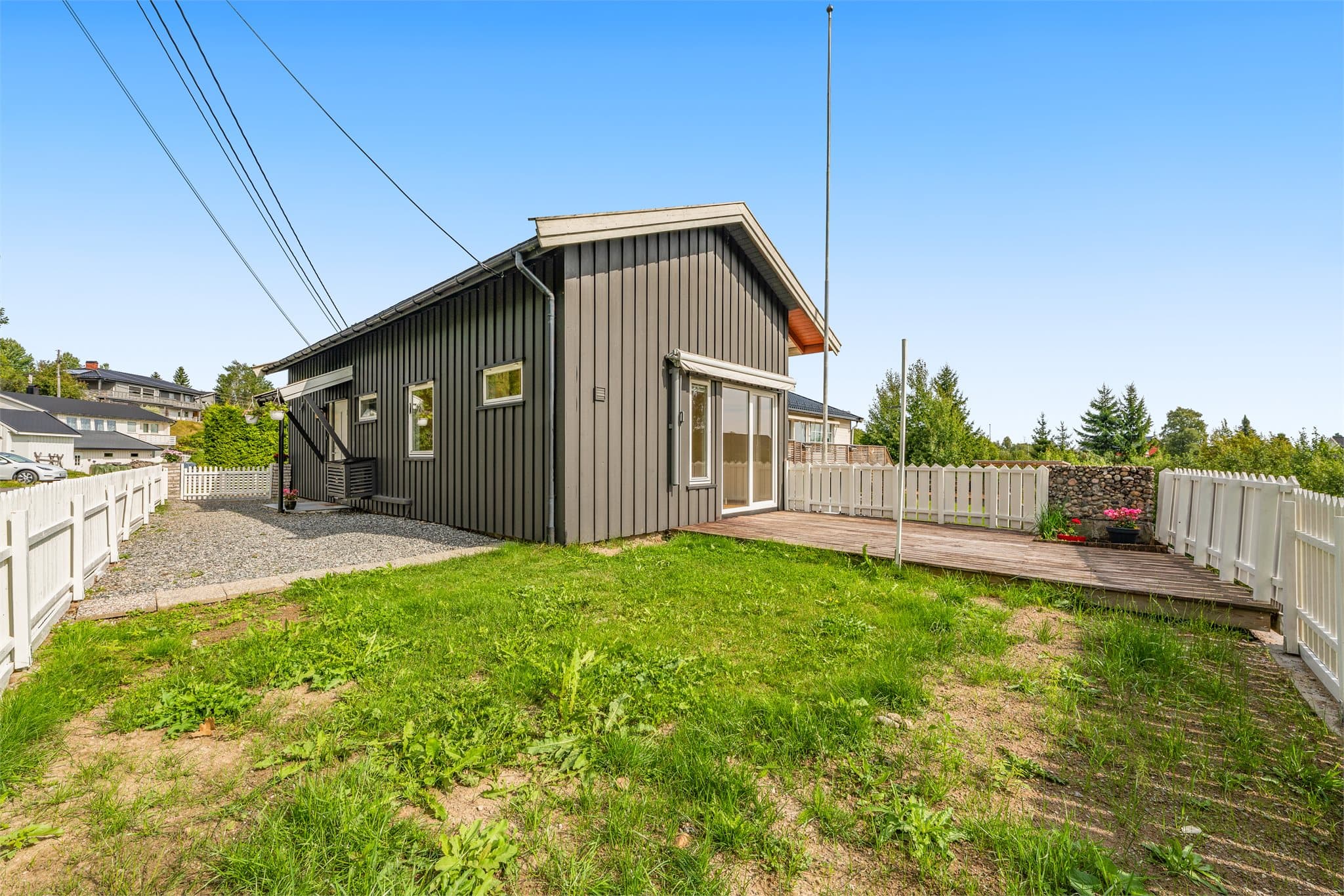 Inngjerdet uteplass med gruset plass, plenareal og markterrasse.