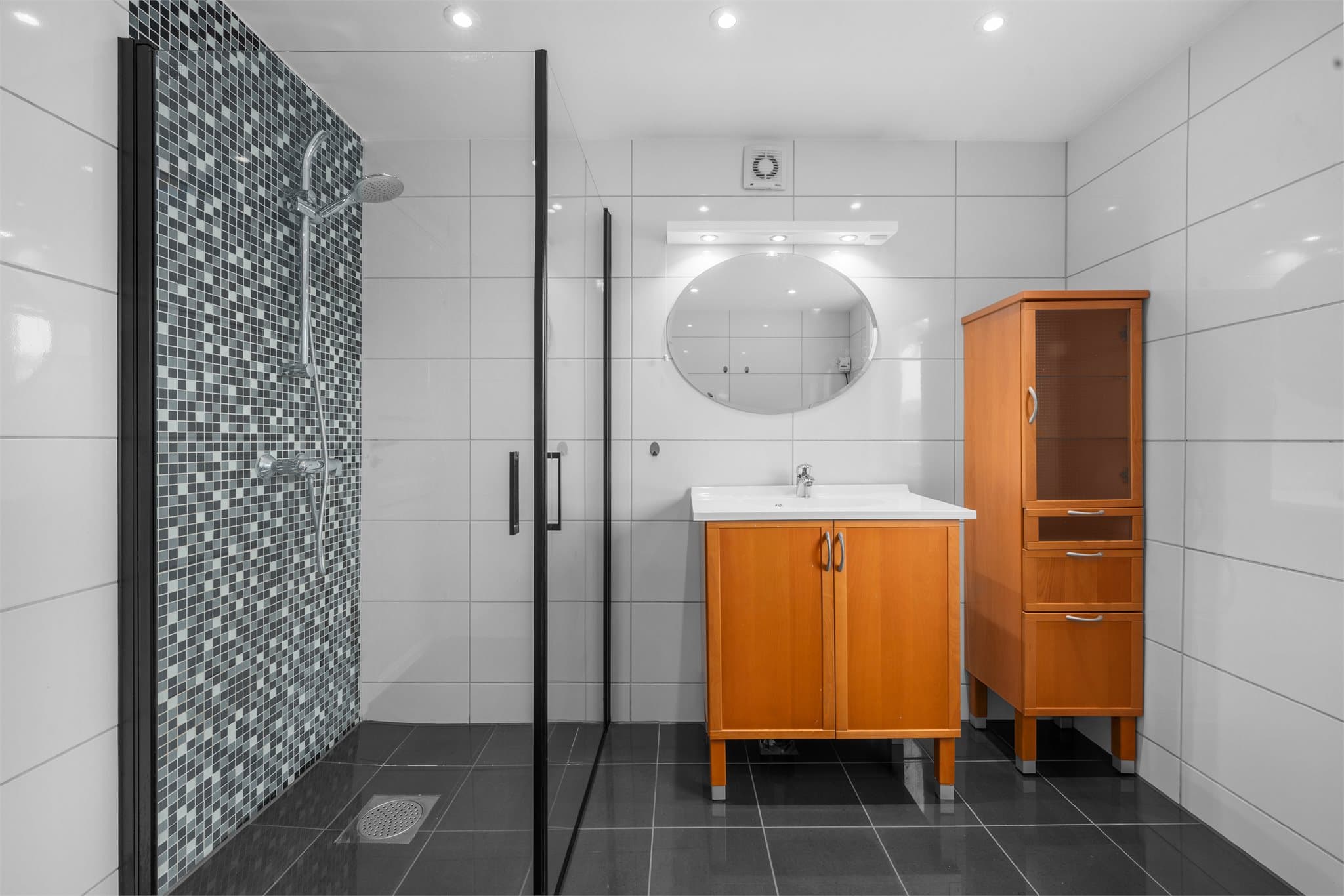 Badet er innredet med servant med underskap, tilhørende speil og høyskap.