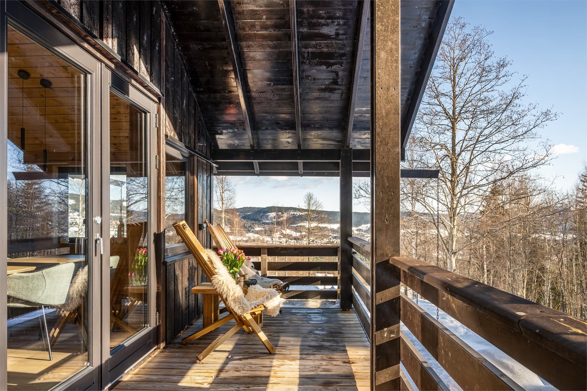 Fra spisestuen og kjøkkenet tar vi turen ut på den romslige, overbygde verandaen som omkranser hytta. Her er det plass til flere sittegrupper, trestoler og grill, og området inviterer til hyggelige måltider ute eller rolige kvelder med utsikt mot naturen.