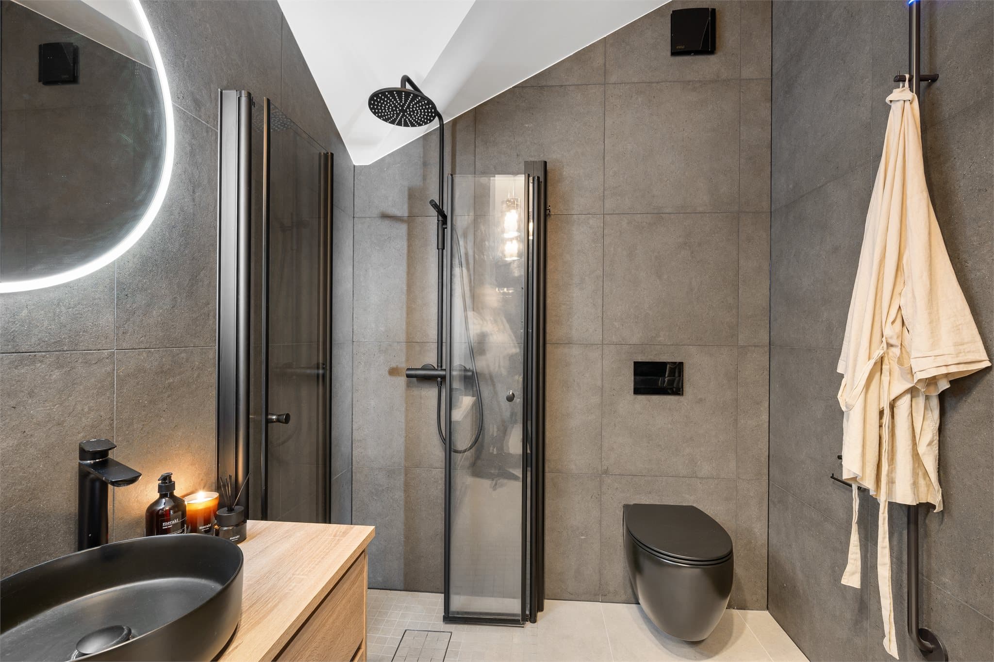 Den sorte vegghengte toalettløsningen, regnfallsdusj med sort armatur og sort servantskål på moderne skuffeinnredning skaper en helhetlig og elegant designlinje.