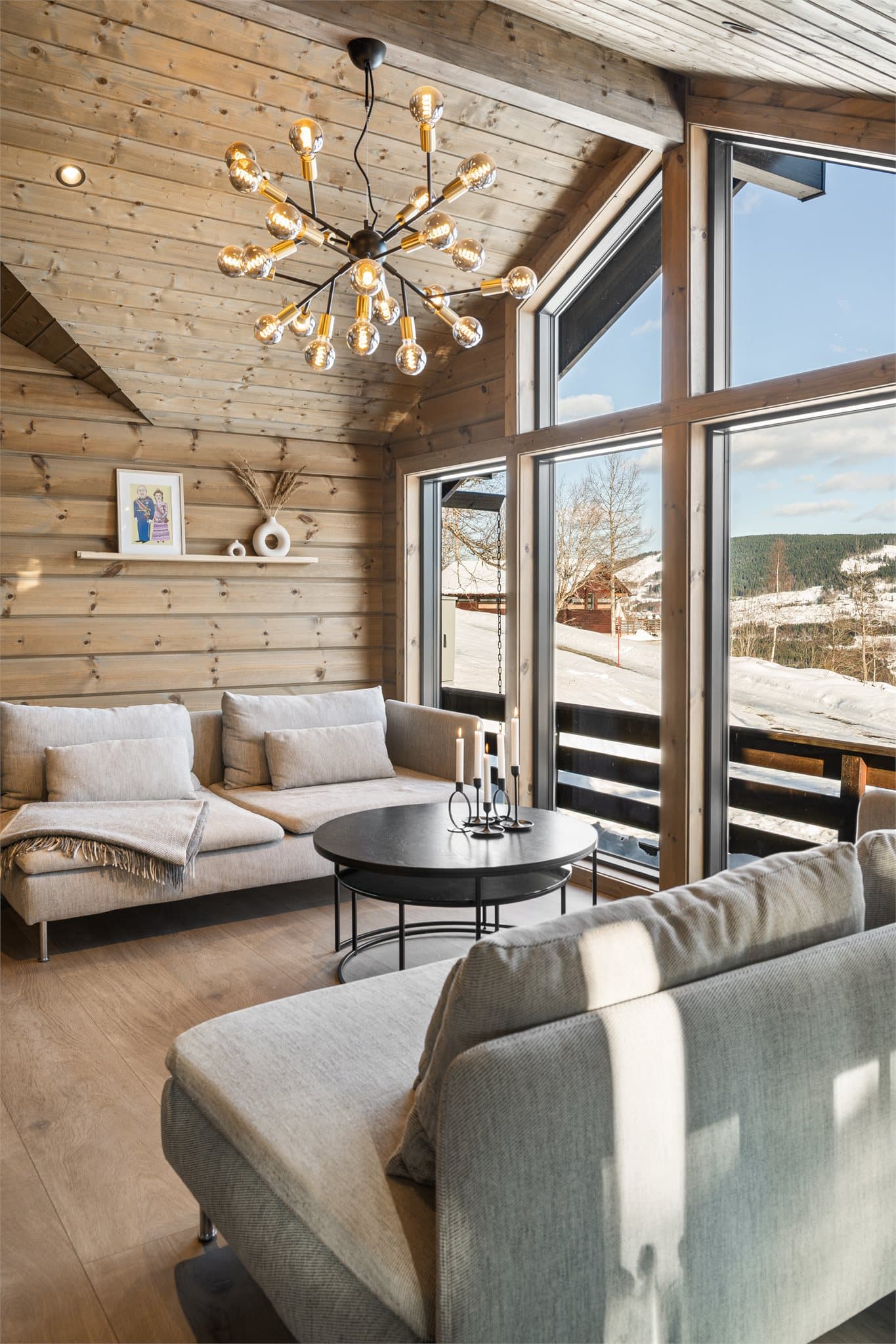 I taket er det integrert moderne downlightsspotter som gir et behagelig og jevnt lys, mens en elegant taklampe henger ned over sofabordet og blir et naturlig blikkfang i rommet.