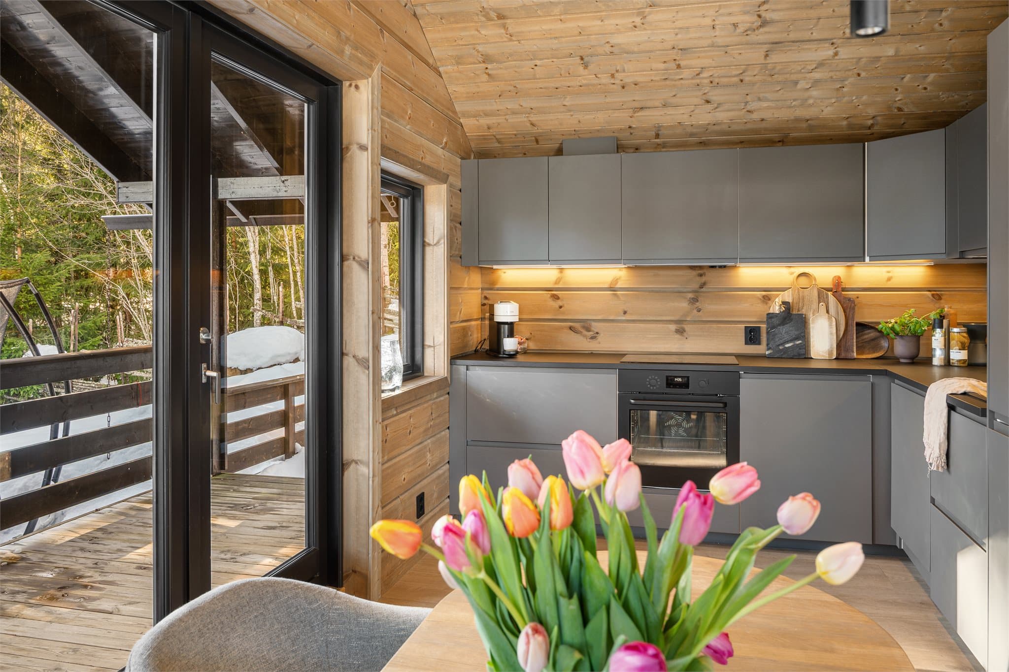 Kjøkkenet fremstår moderne og stilrent med slette, grå fronter som gir et tidløst og elegant uttrykk. Den praktiske laminatbenkeplaten gir gode arbeidsflater og tåler hyttelivets bruk godt, samtidig som den harmonerer fint med de rolige fargetonene.