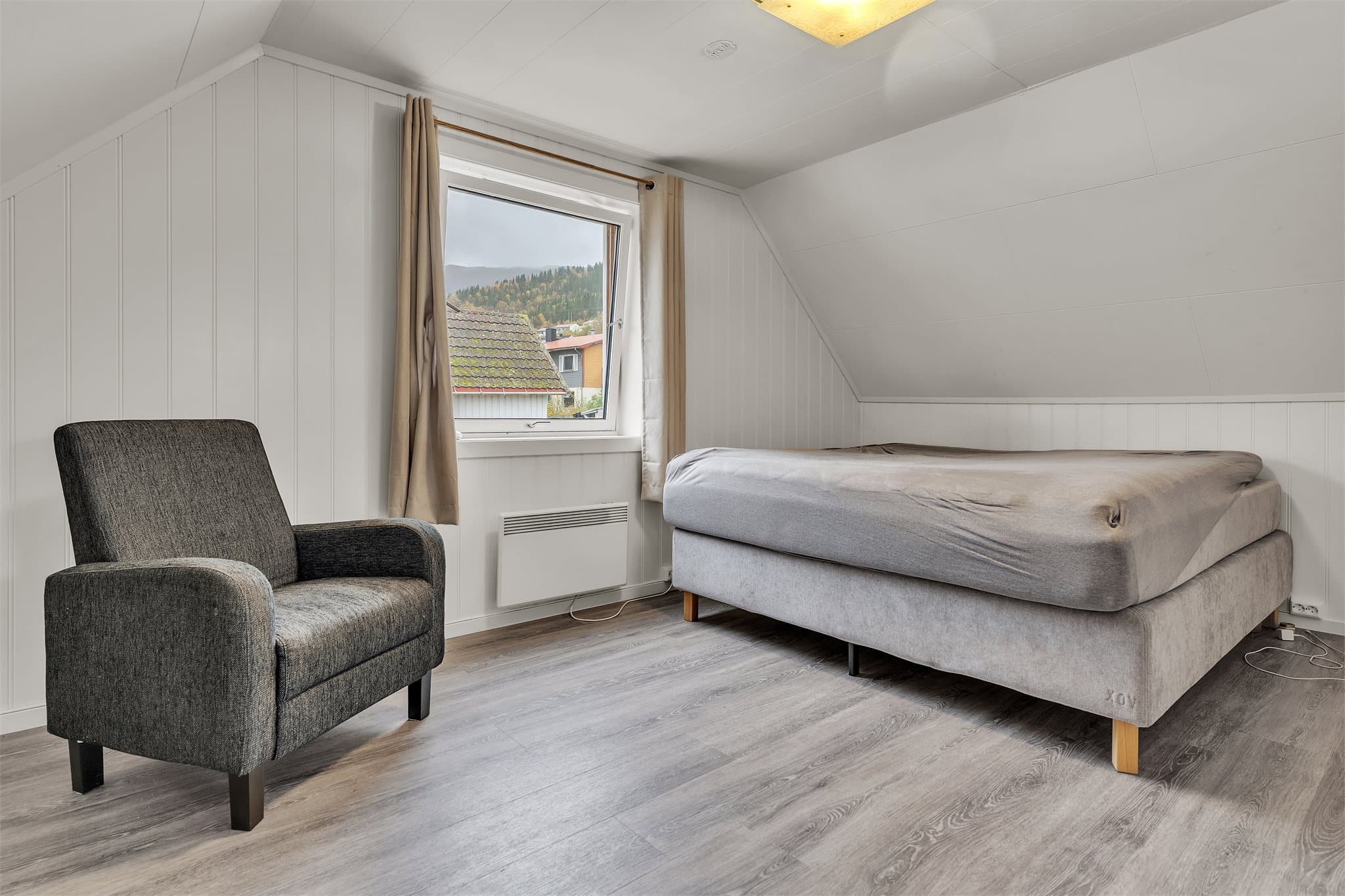 Innredet loftsrom med skråtak, laminatgulv og panelkledde overflater.