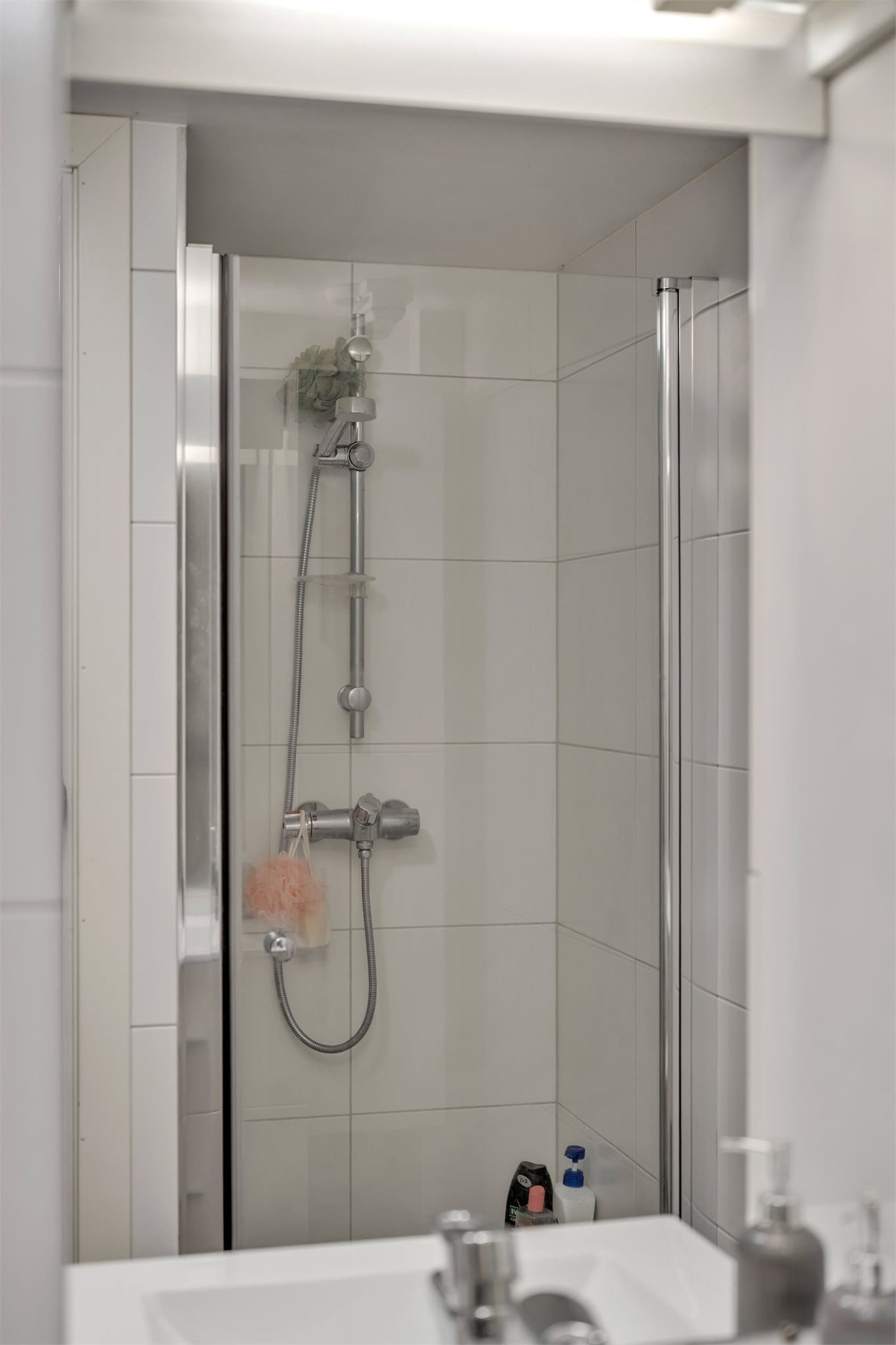 Dusjhjørne med innfellbare glassdører og flislagte overflater.