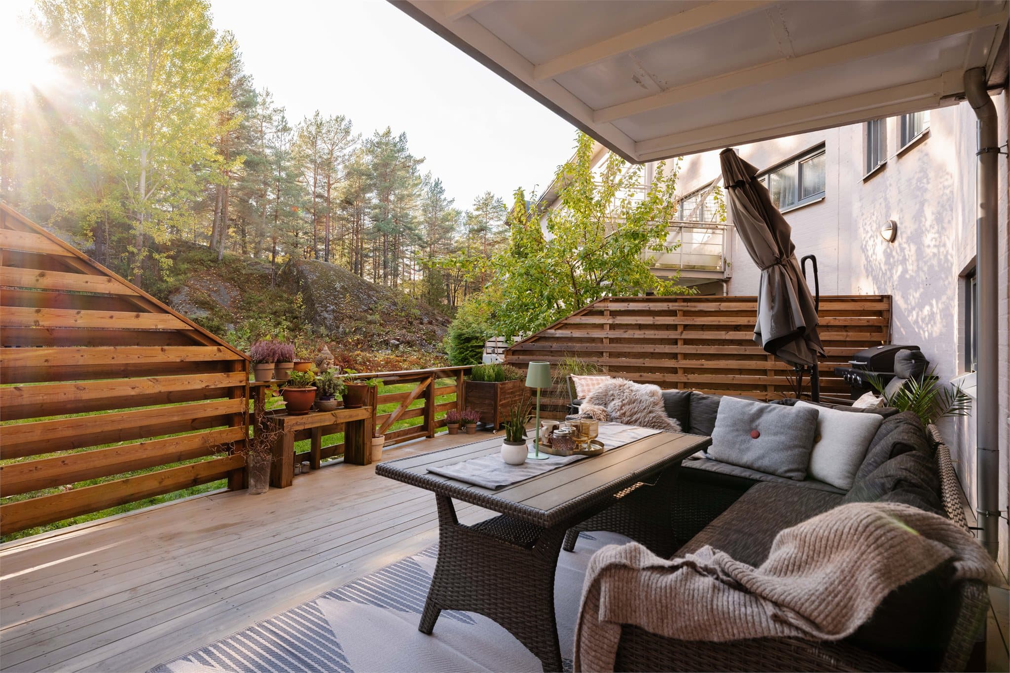 Romslig terrasse med terrassebord i tre, skjermende levegger og frodig beplantning som skaper en lun og privat uteplass.