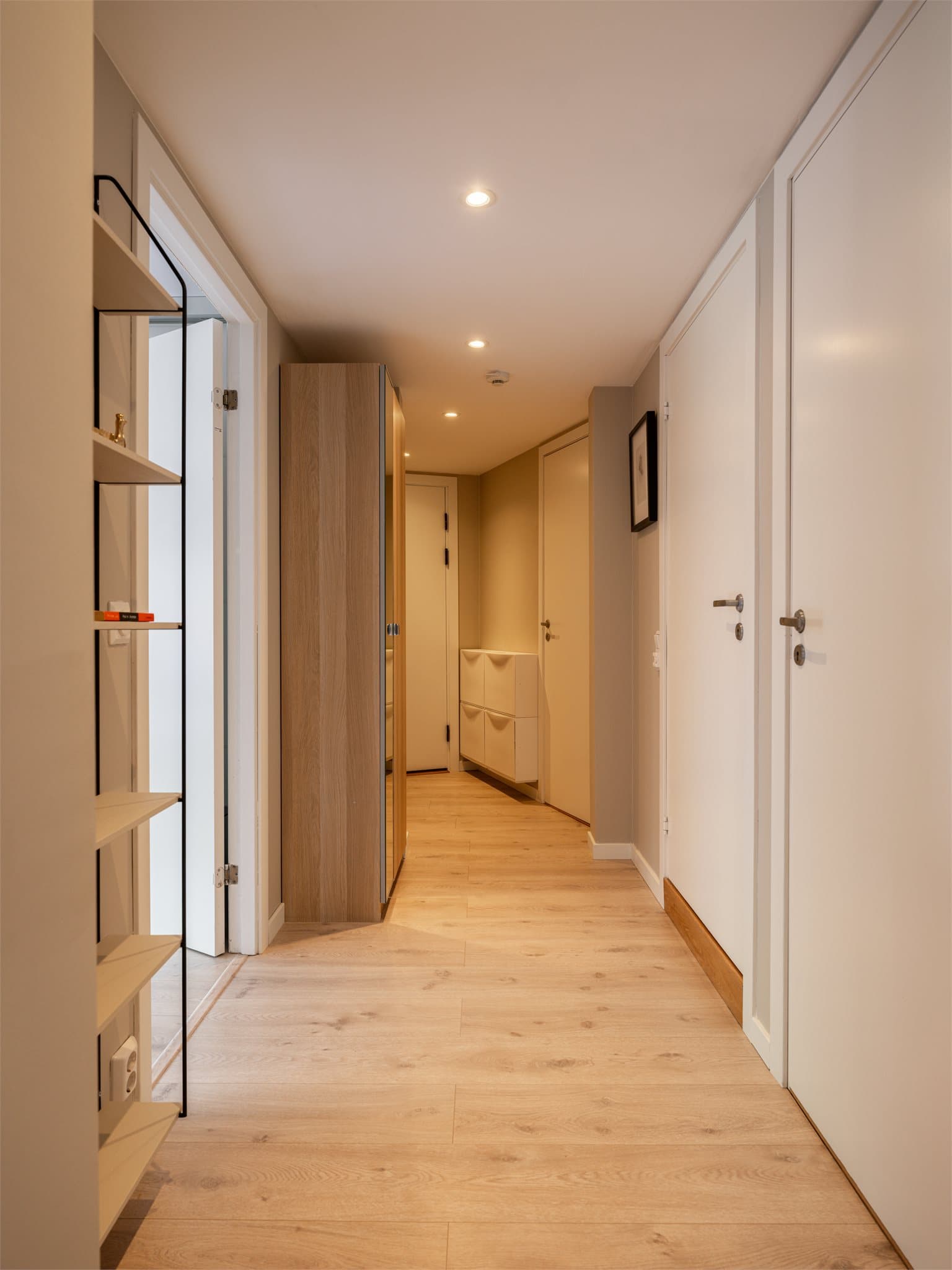Gangen har et lyst og helhetlig uttrykk med gjennomgående gulv og downlights i taket. Det er gode oppbevaringsmuligheter med skap og hyller langs veggene.